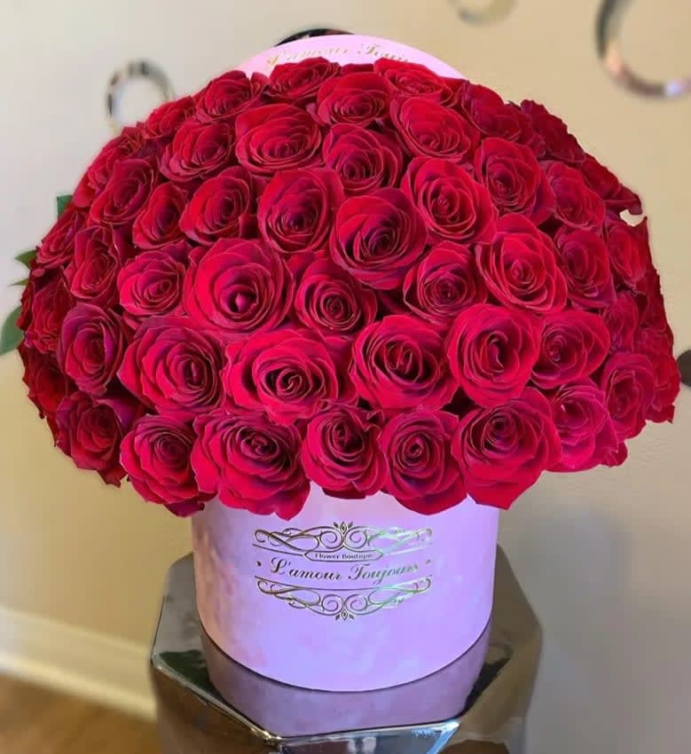Large dome of red roses arranged in a pink round hat box with gold script on the front