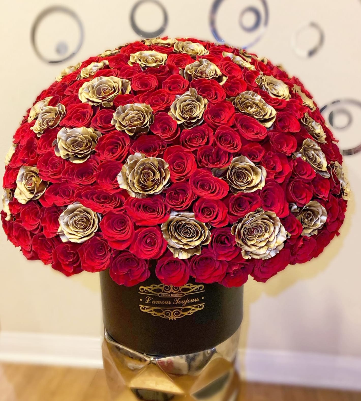 Large dome of red and gold roses arranged in a black hat box on a metallic pedestal
