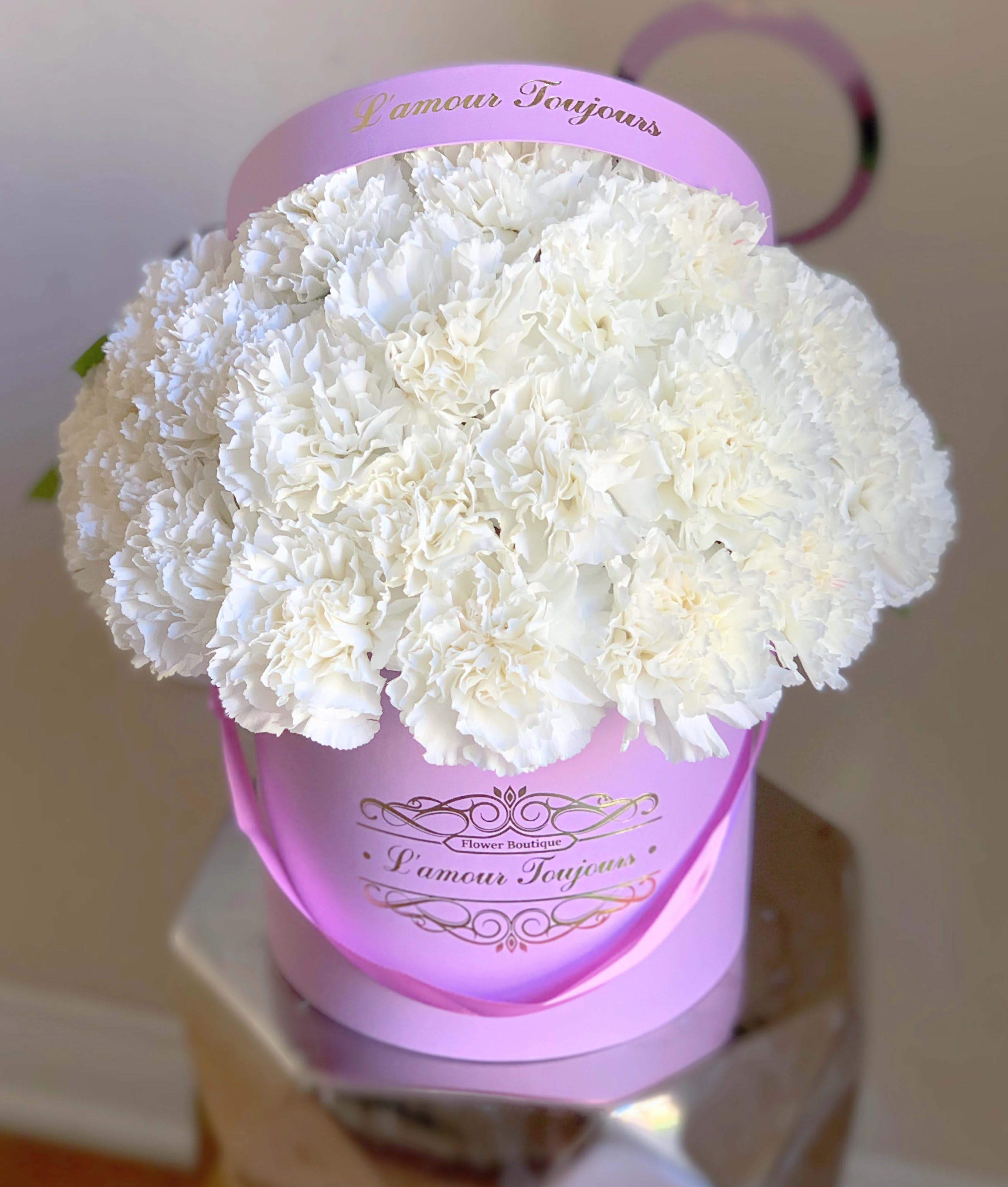 White carnation bouquet in a pink hatbox with ribbon handle