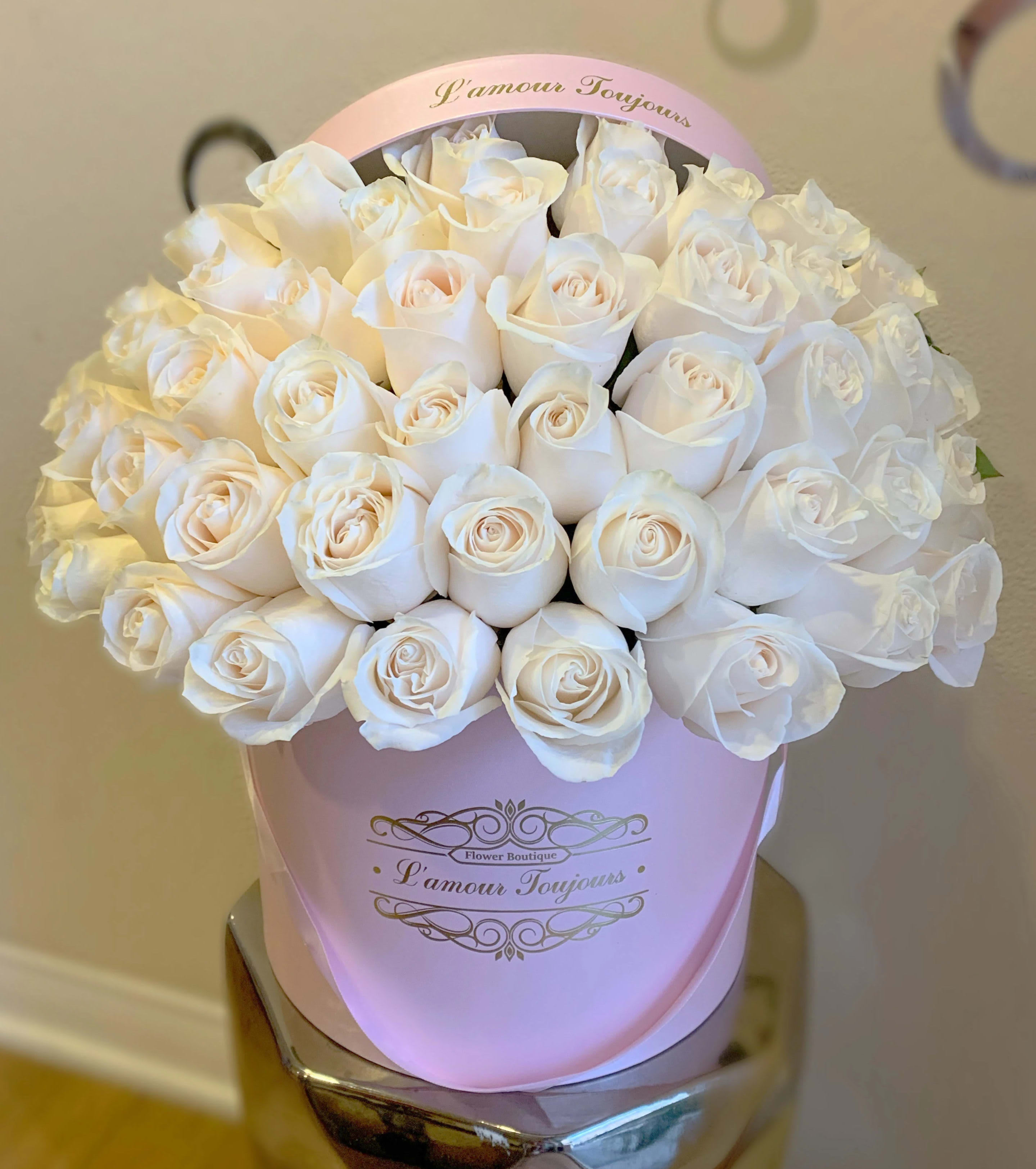 Round box of pale ivory roses densely arranged in a light pink hatbox