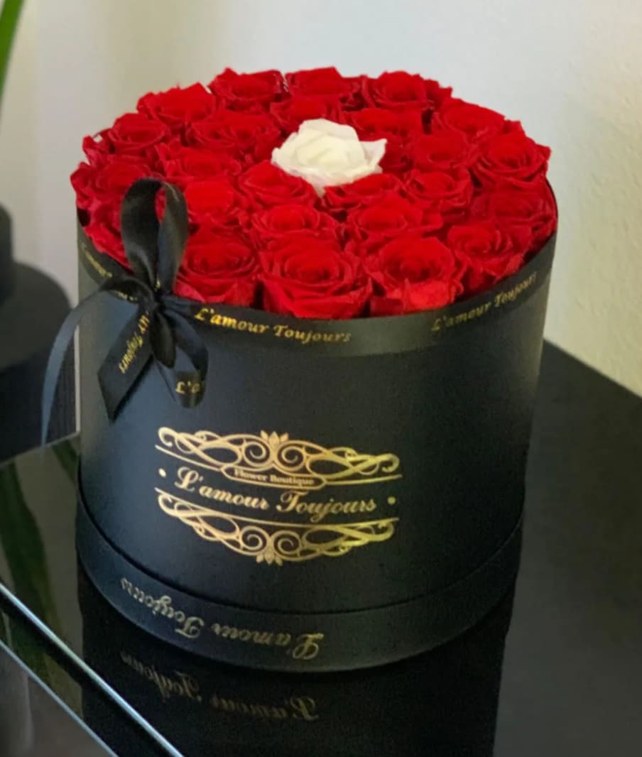 Round box of red roses with one white rose on top and a black ribbon