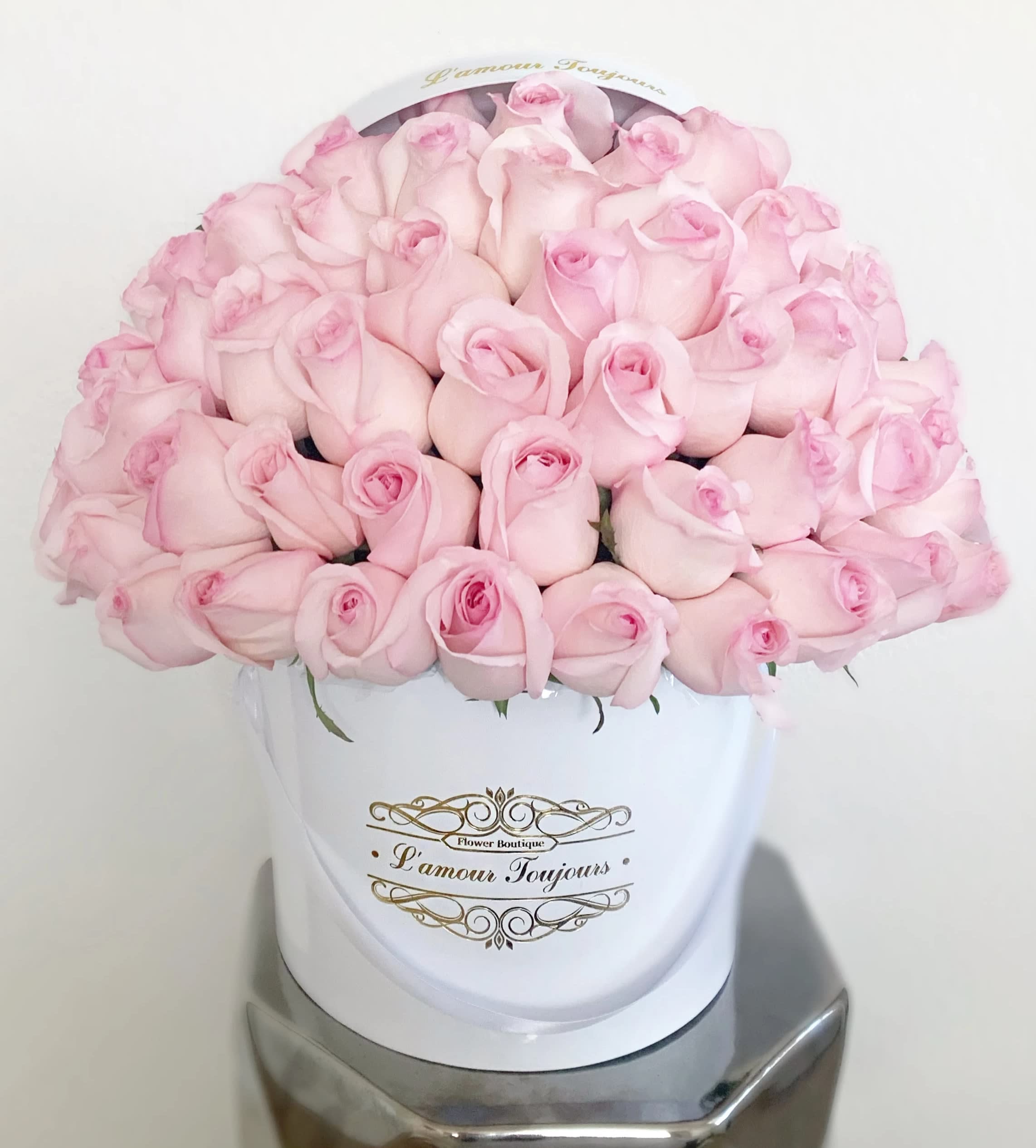 Round box of pale pink roses tightly arranged in a white hatbox with gold script label