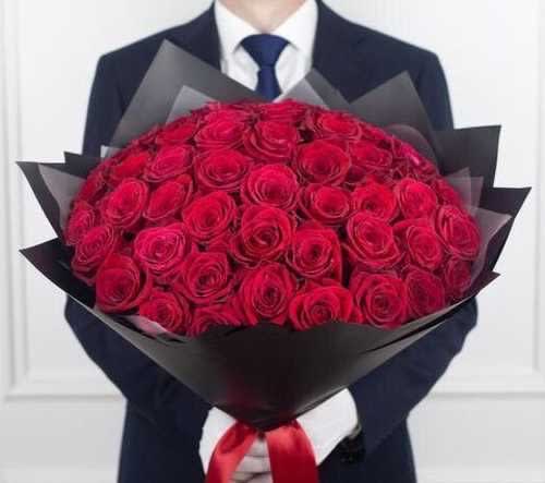 Large bouquet of tightly packed red roses wrapped in black paper, held by a person in a dark suit.