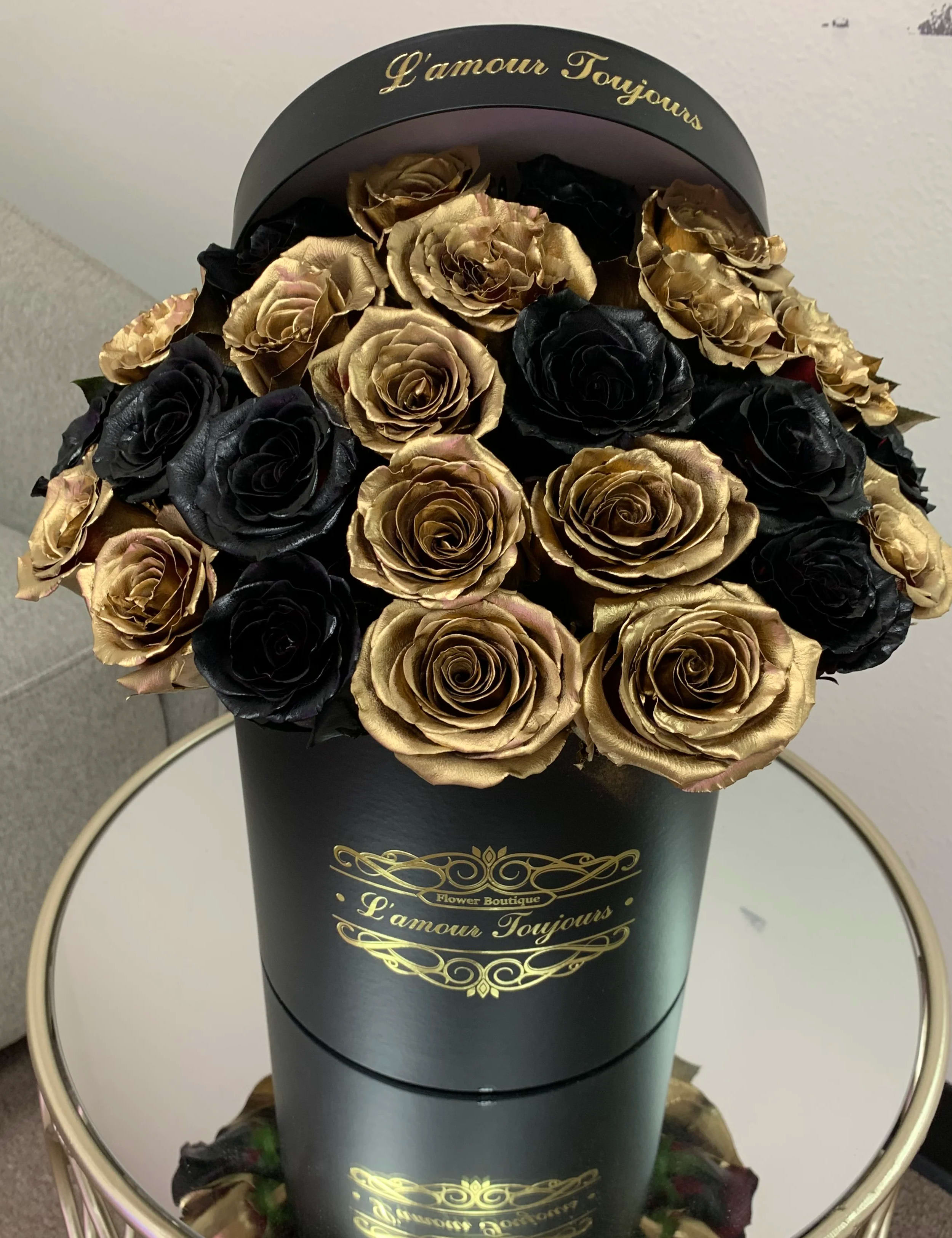 Black and gold roses arranged in a tall black hat box with gold lettering