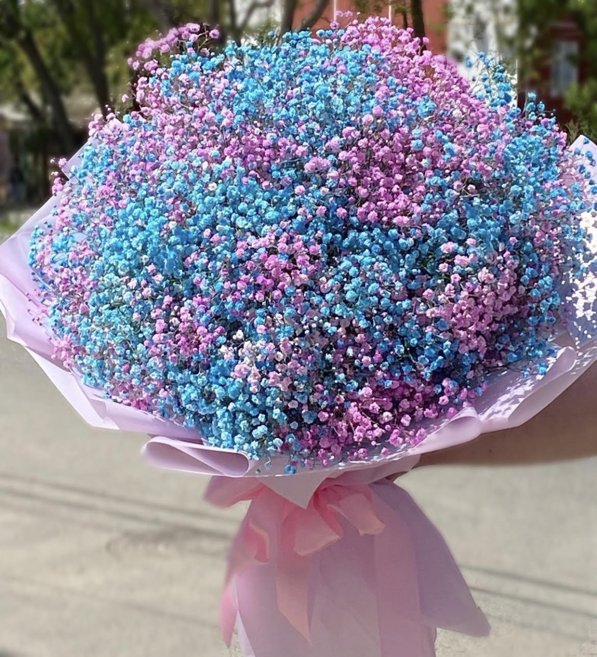 Large round bouquet of blue and pink tiny blooms wrapped in pale pink paper with a bow