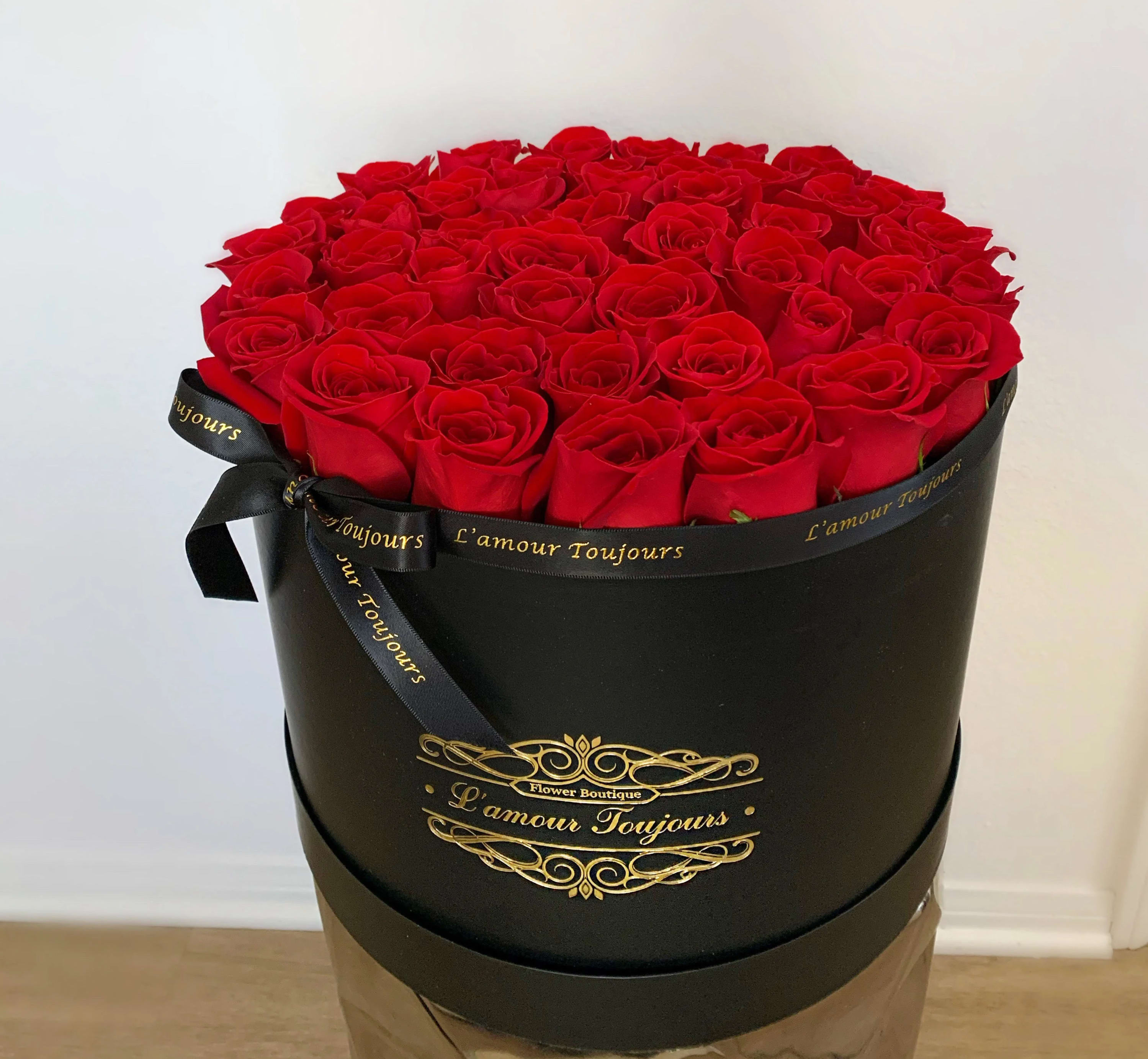 Round box filled with red roses and tied with a black ribbon