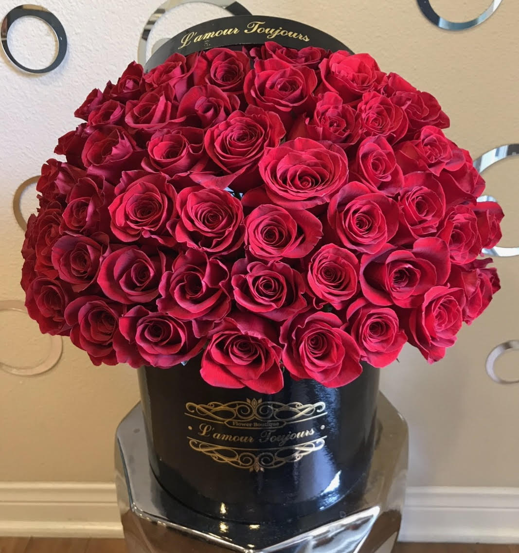 Large dome of red roses arranged in a round black hatbox with gold lettering.