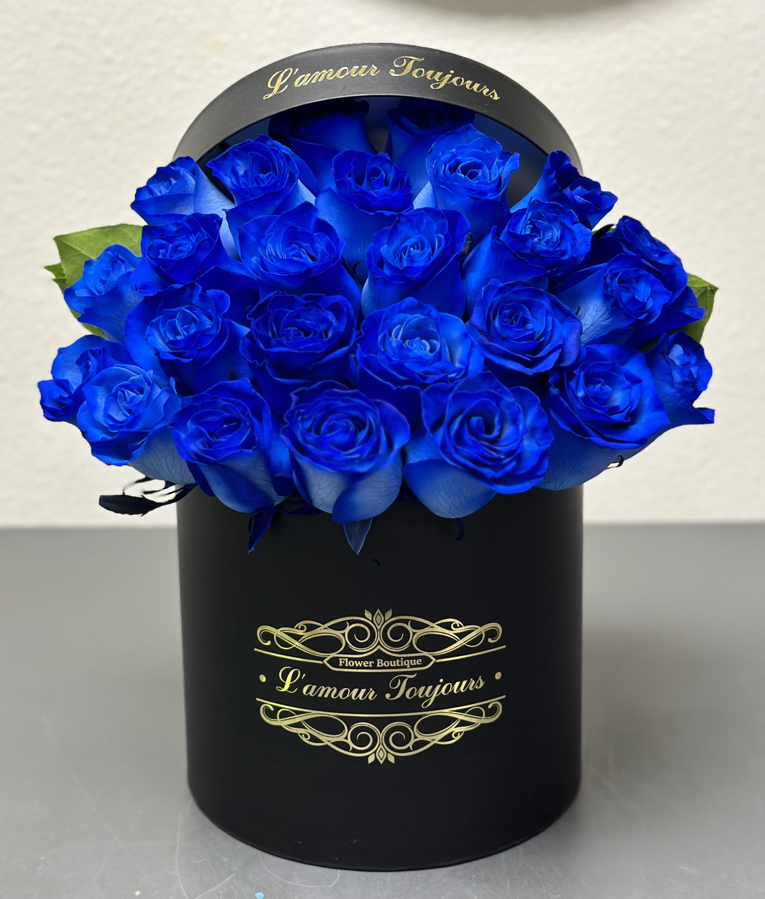 Round hatbox of vivid blue roses in a black cylinder container with gold script.