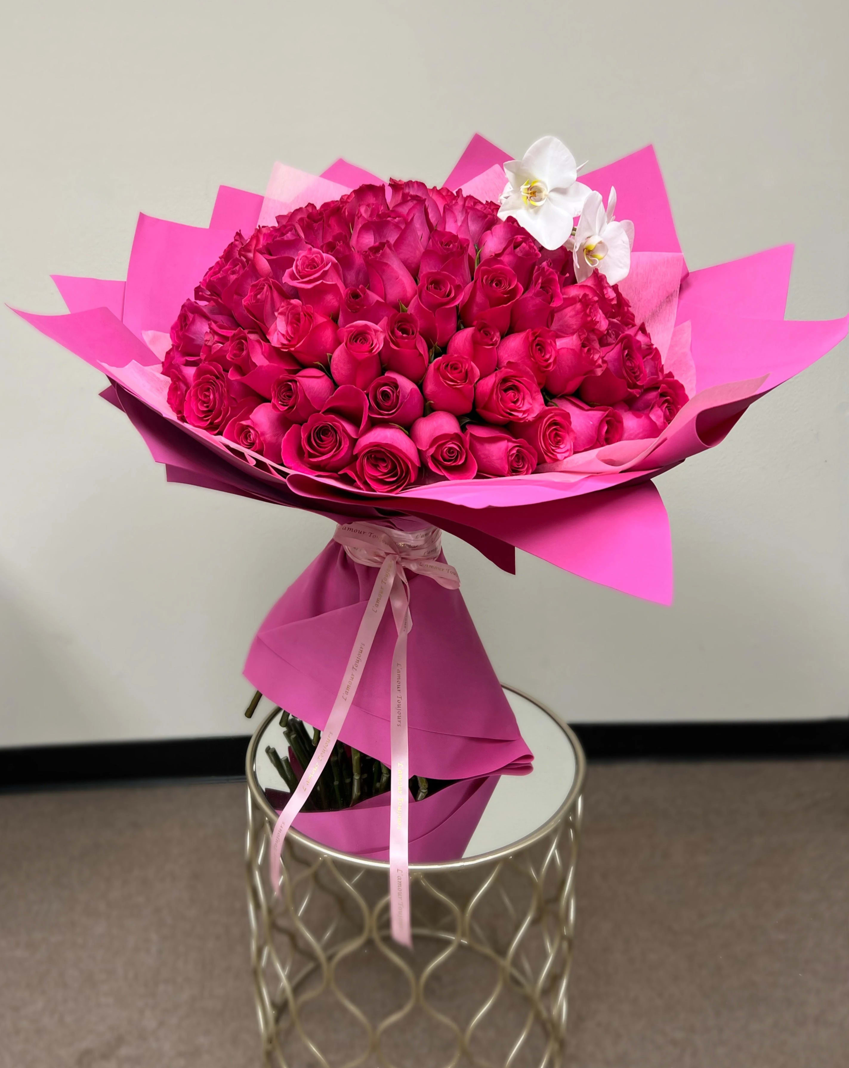 Large bouquet of hot pink roses with white orchids wrapped in bright pink paper