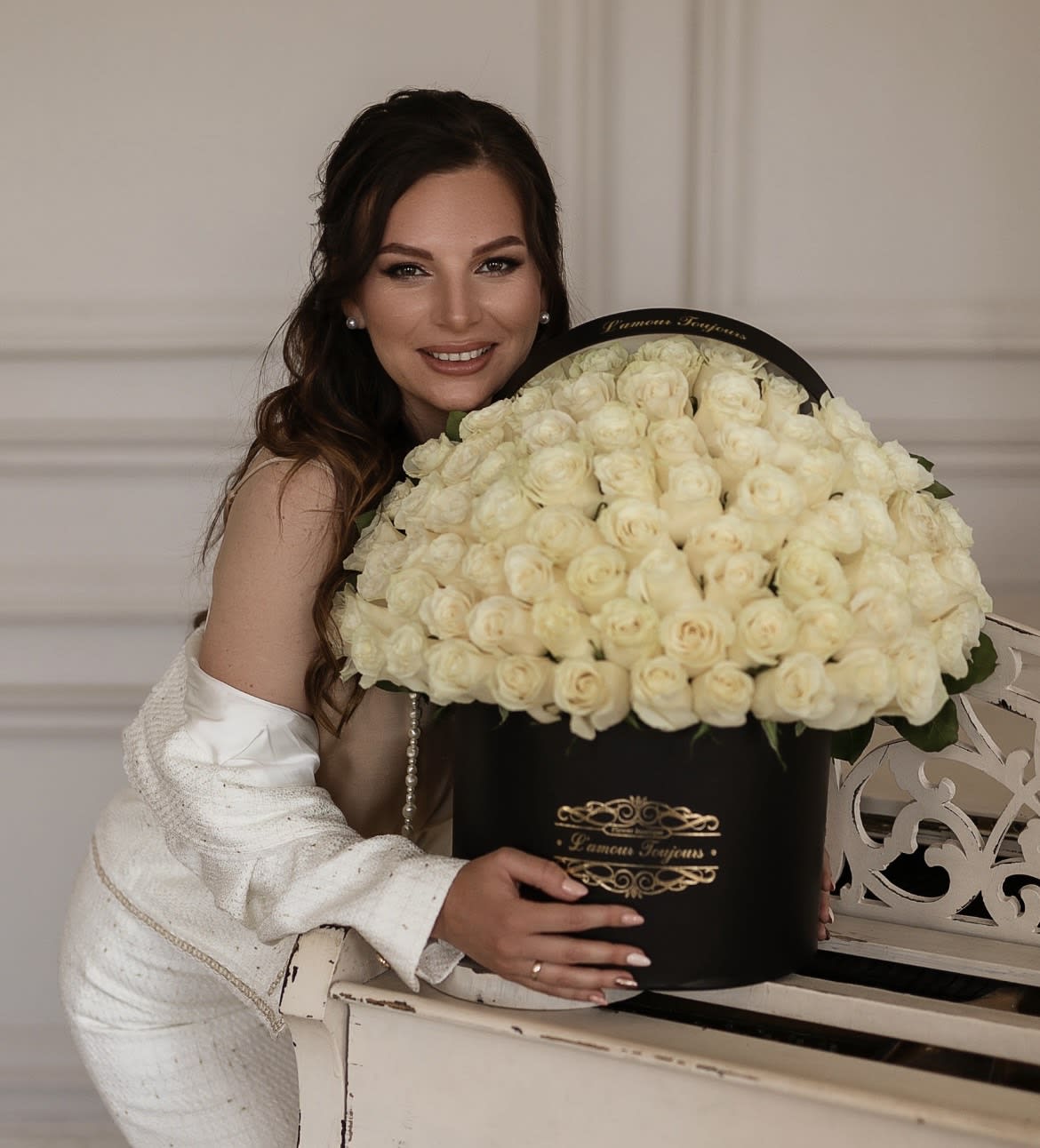 Large black hatbox filled with cream roses beside a smiling woman in white.