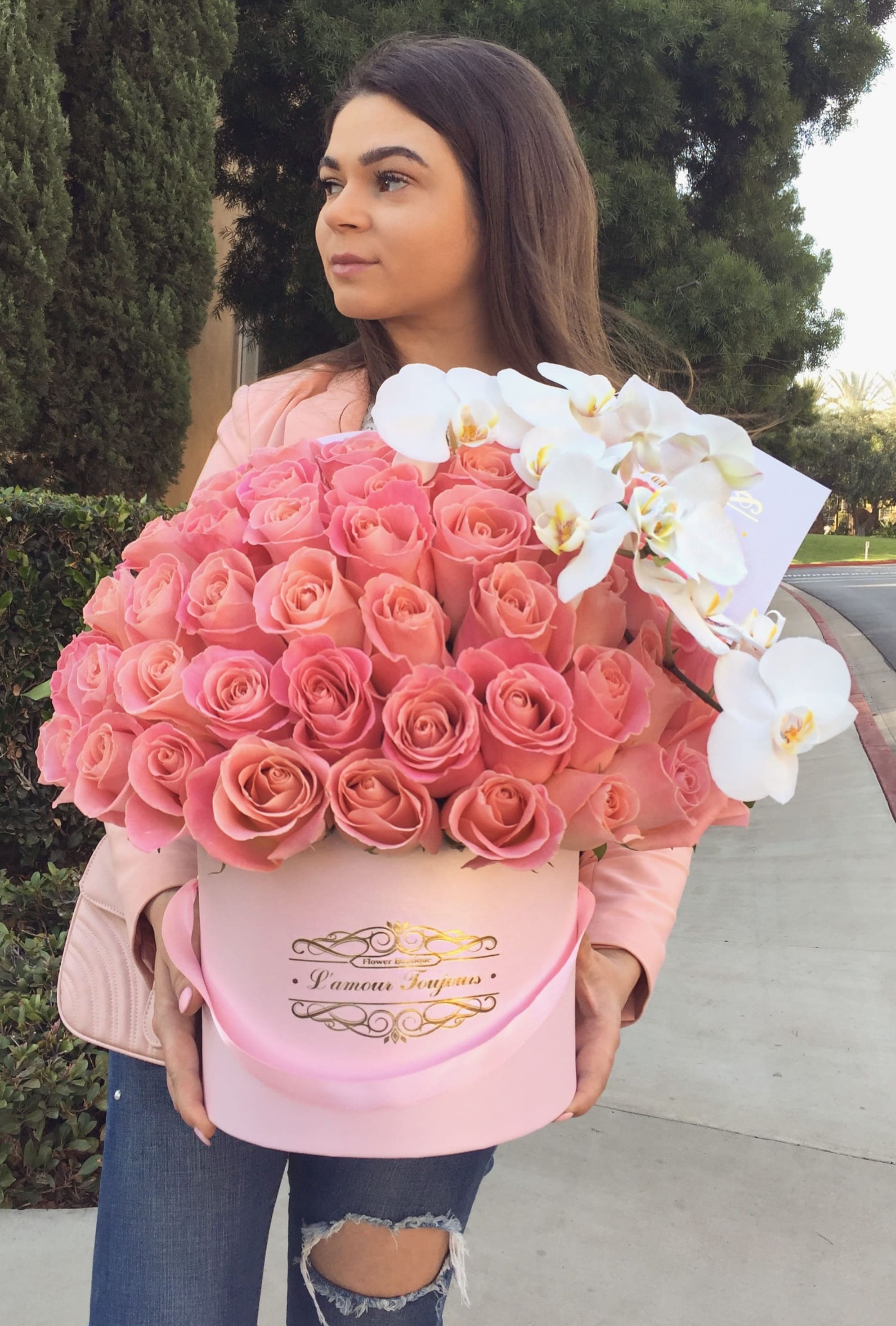 Large round pink hatbox of pink roses with white orchids, held by a person outdoors