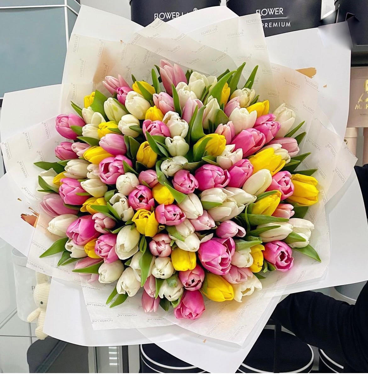 Large bouquet of pink, white, and yellow tulips wrapped in white paper