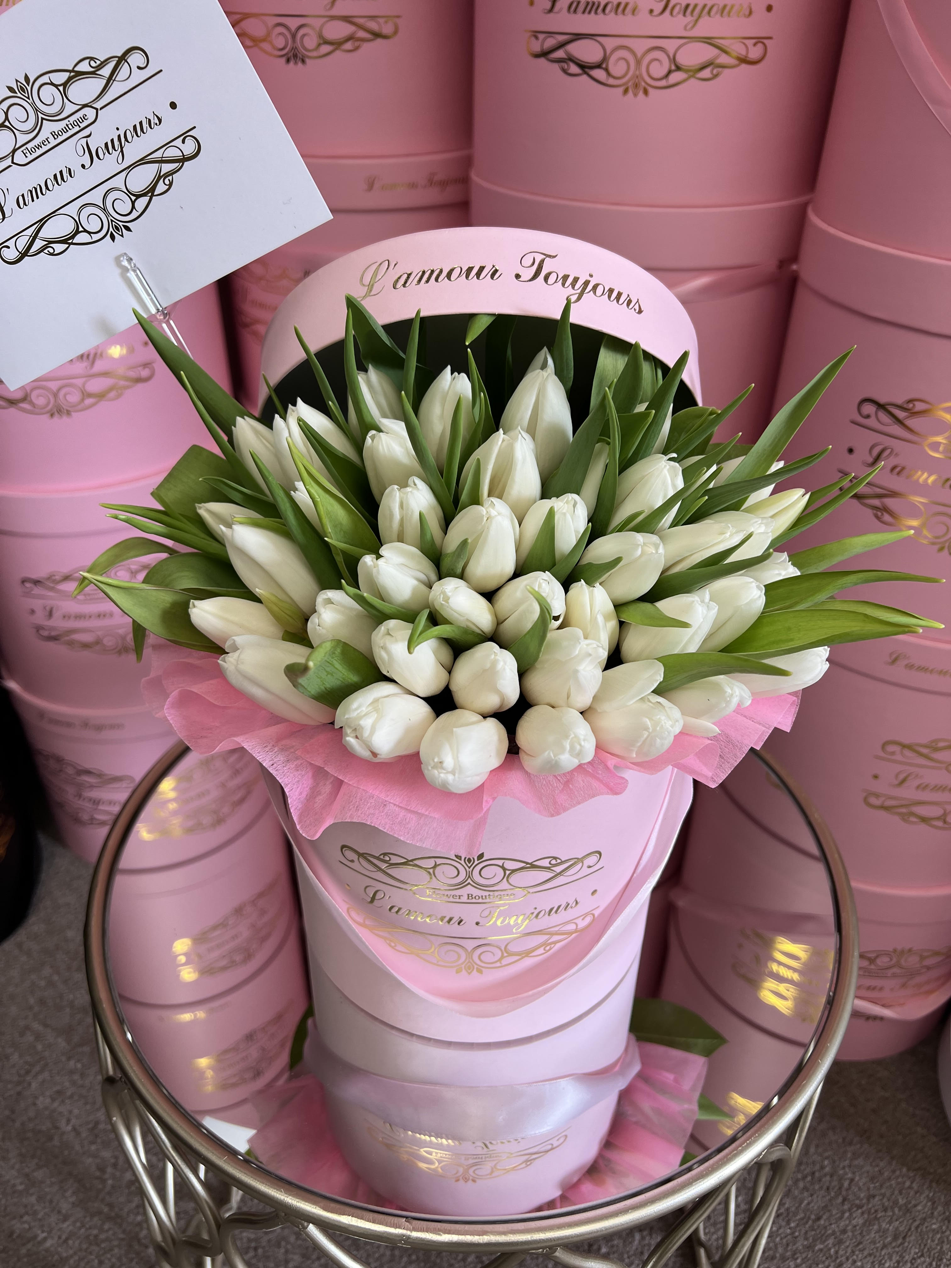 White tulips arranged in a pink hat box with green leaves