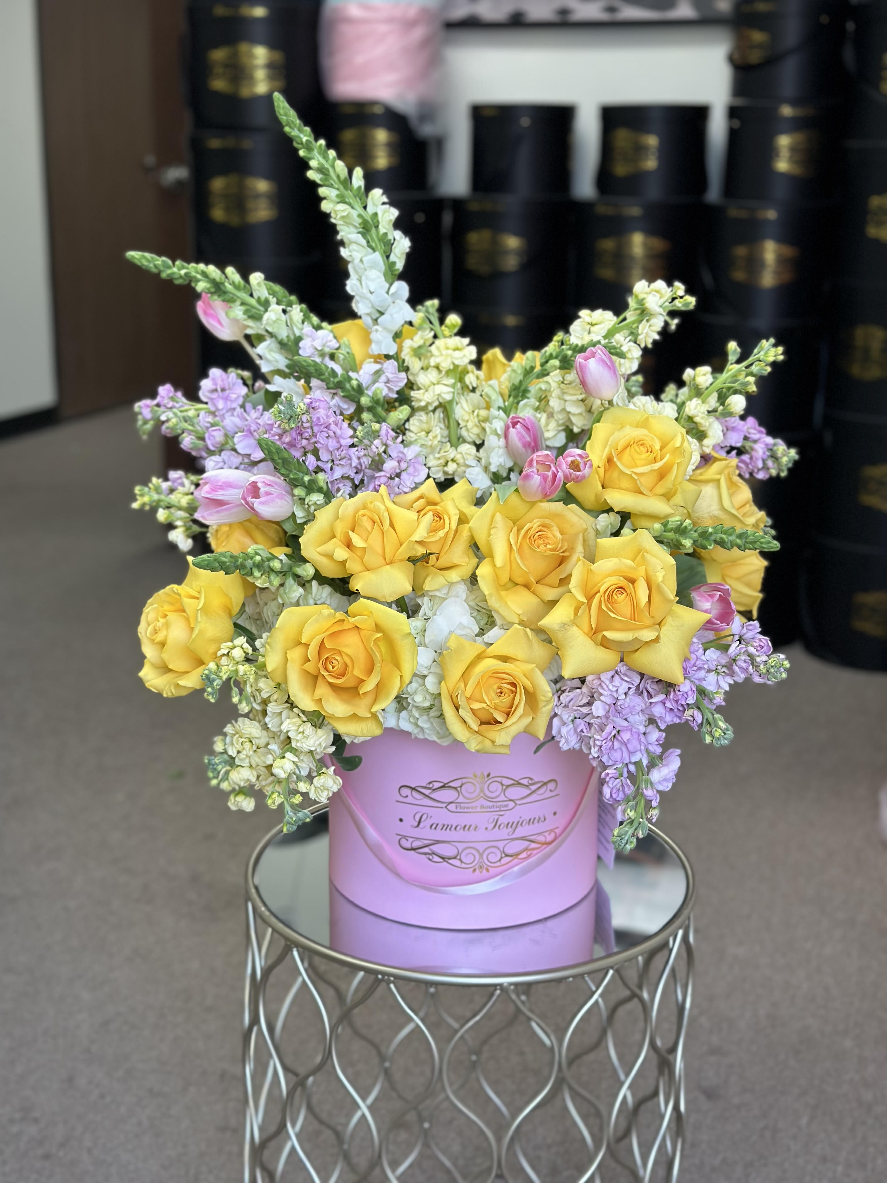 Yellow roses and lavender flowers arranged in a pink hat box