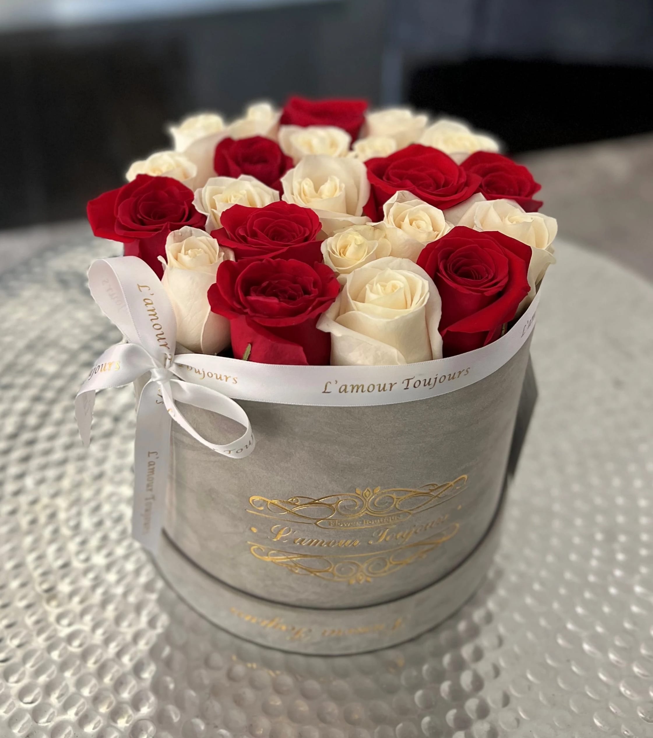 Round box of red and white roses arranged tightly in a gray hatbox with white printed ribbon.