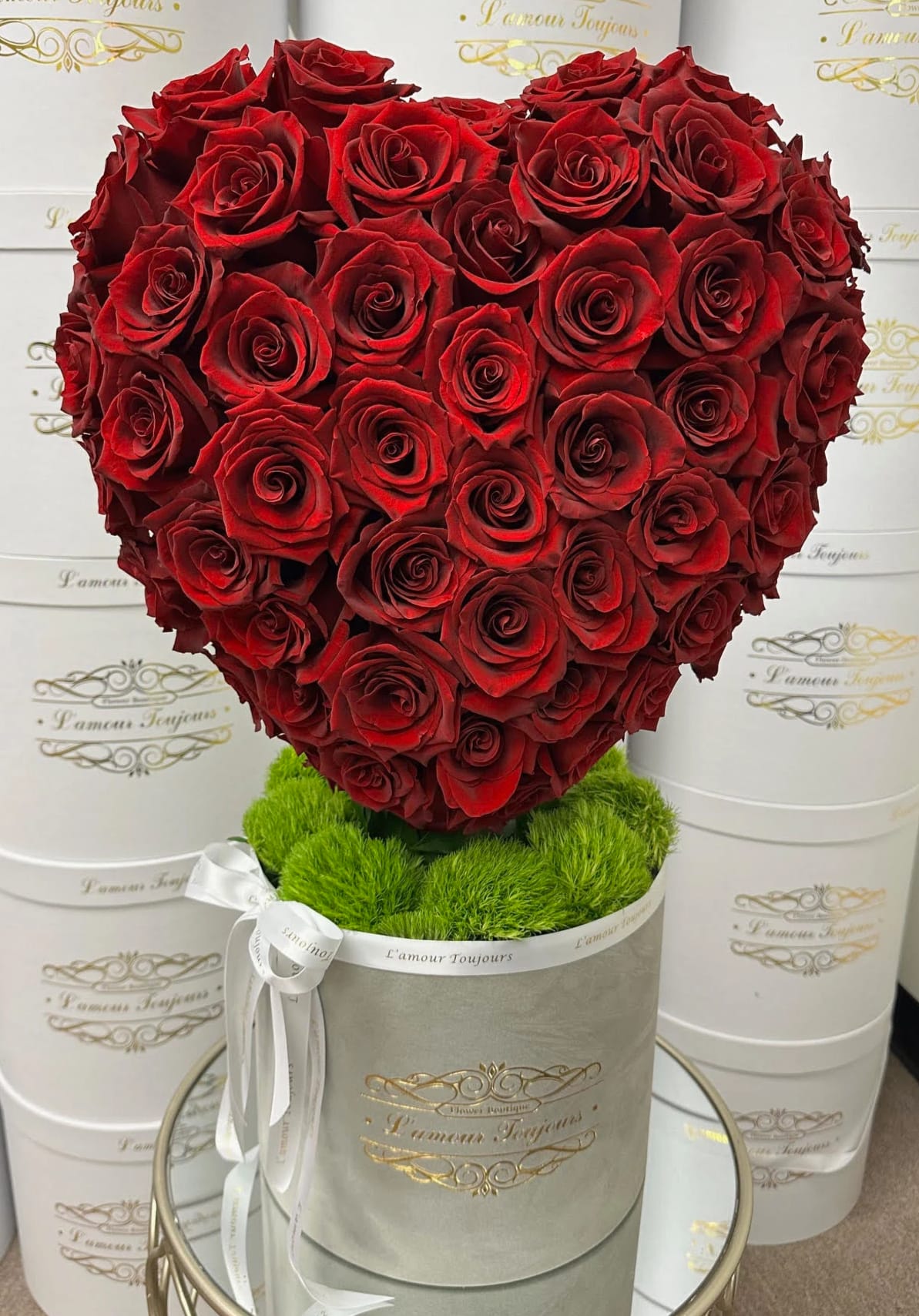 Heart-shaped arrangement of red roses in a round box with green moss and a white ribbon
