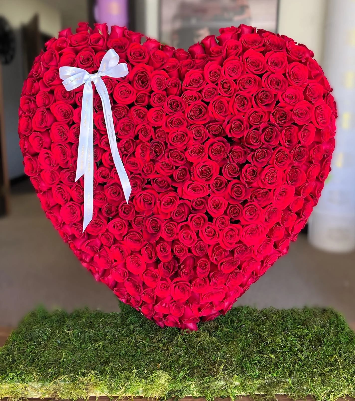 Heart-shaped arrangement of red roses with a white ribbon bow