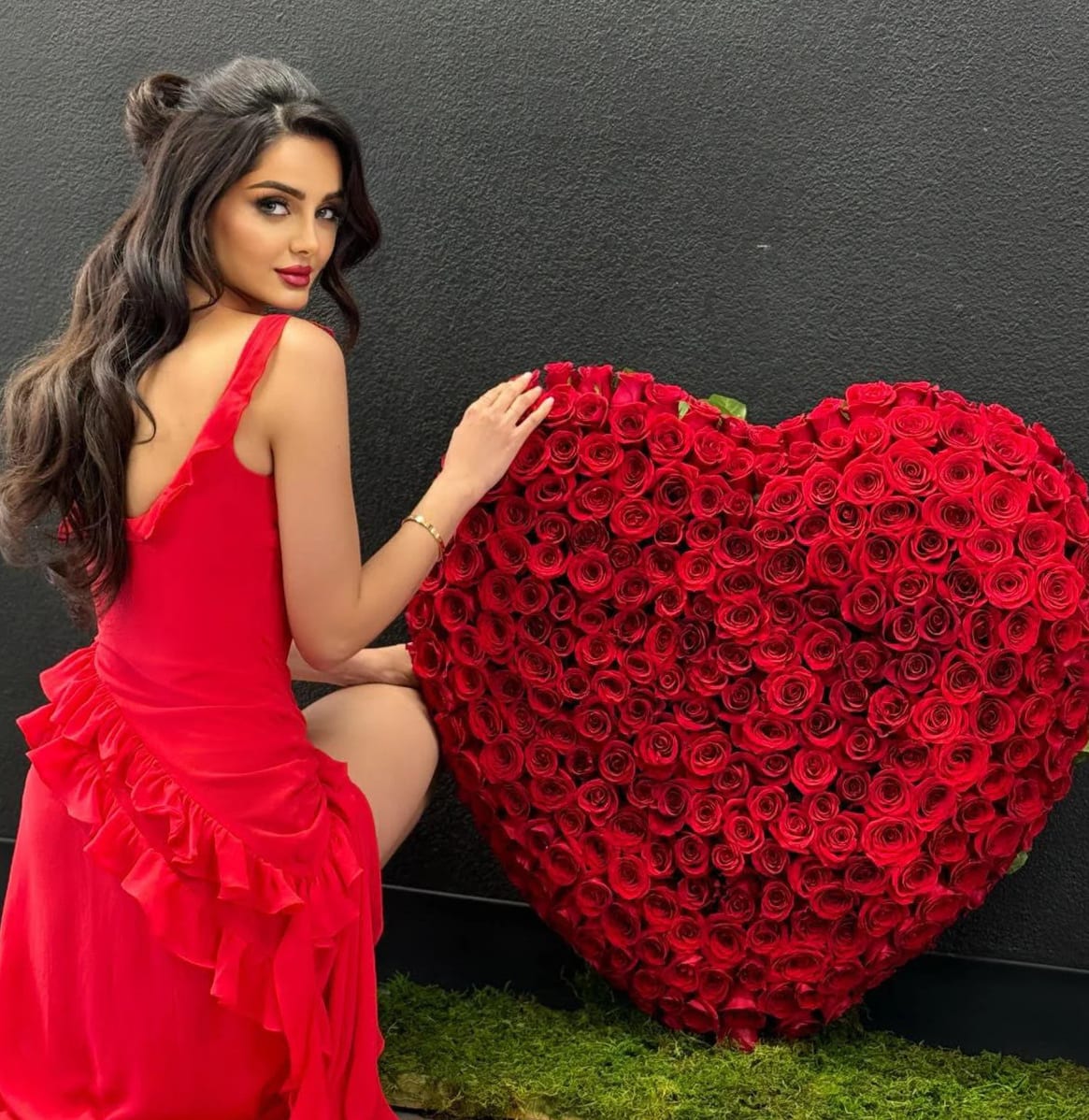 Woman in a red dress posing beside a large heart-shaped rose arrangement