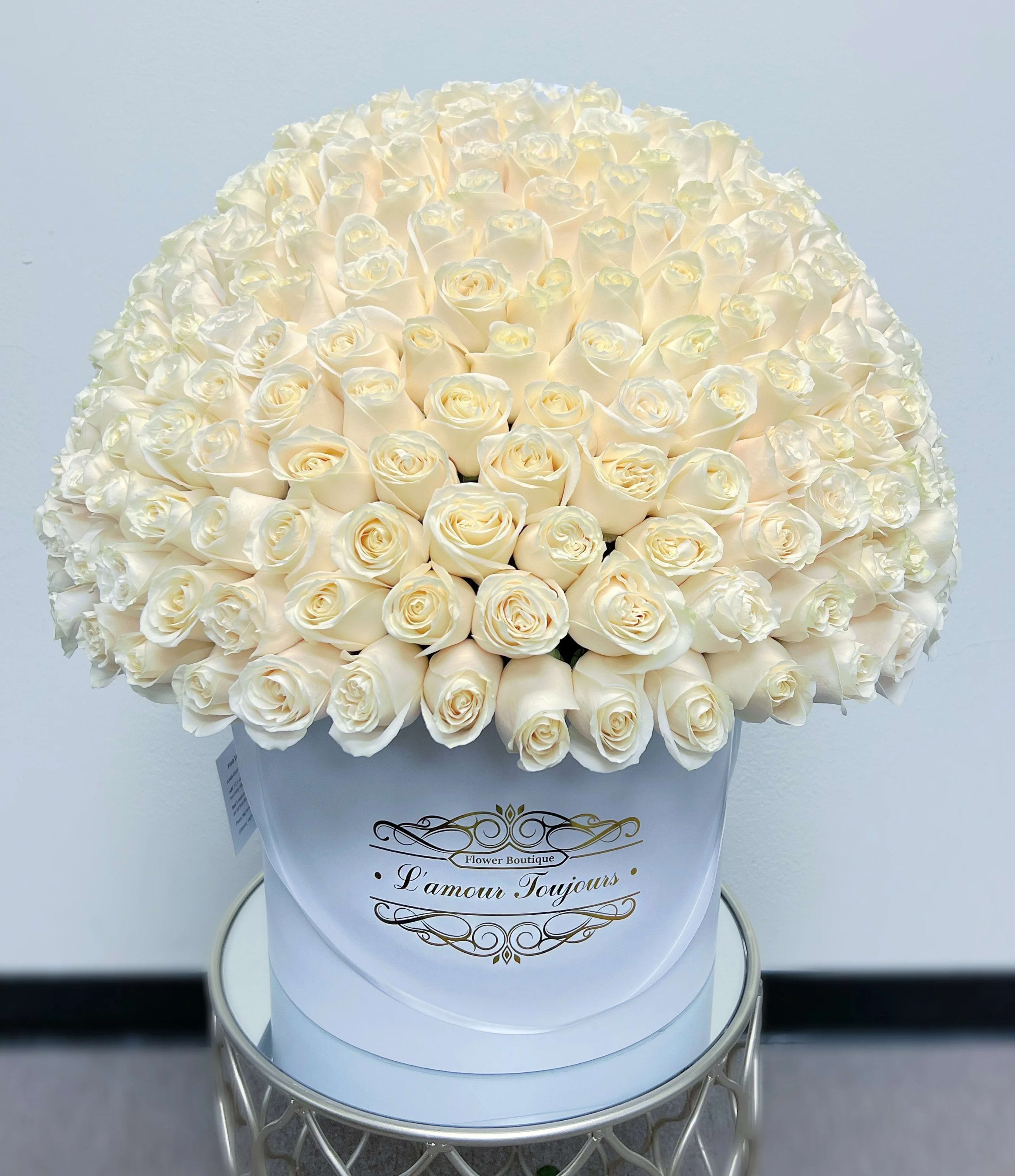 Large dome of cream roses arranged in a white hat box on a small table