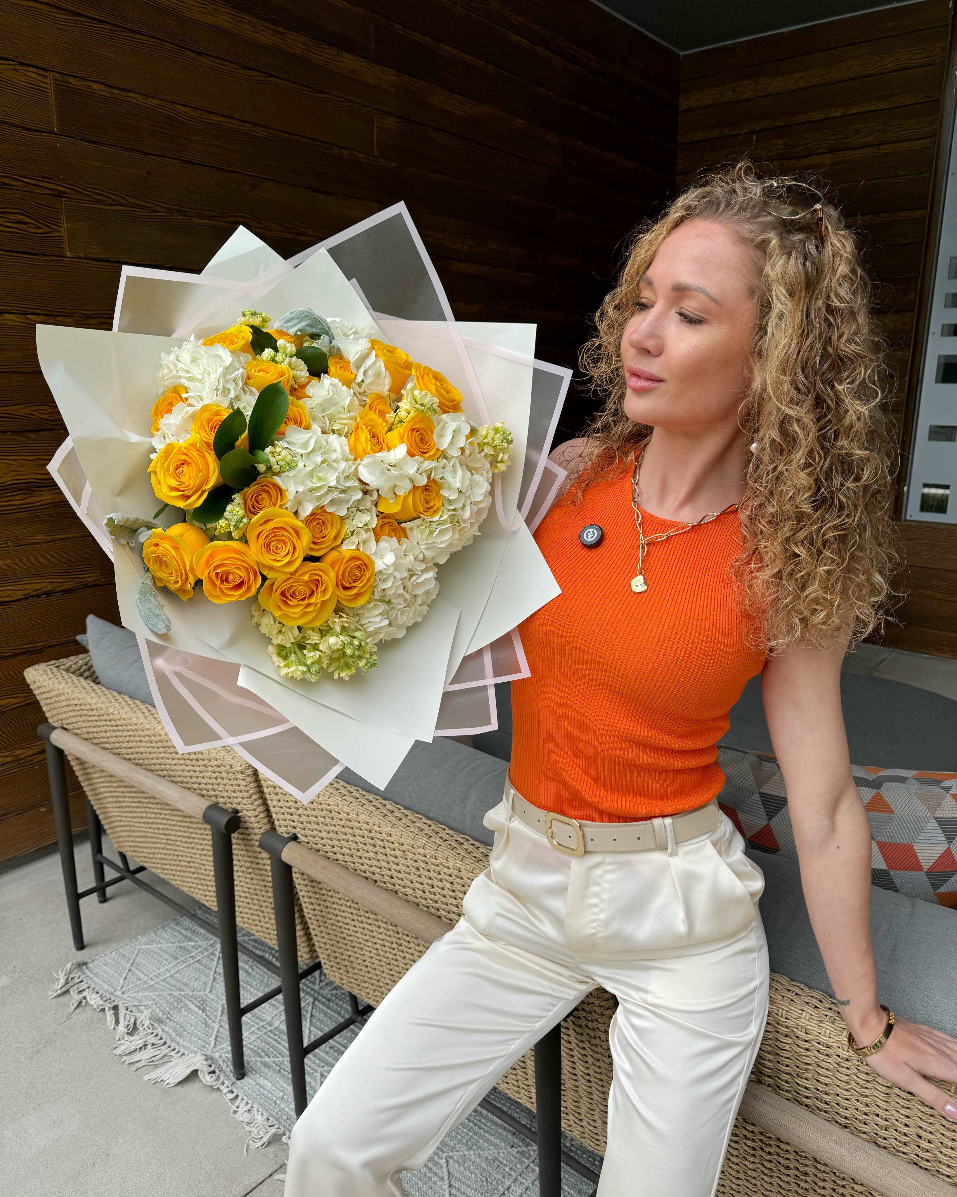 Large bouquet of yellow roses and white hydrangeas wrapped in white paper, held by a person.