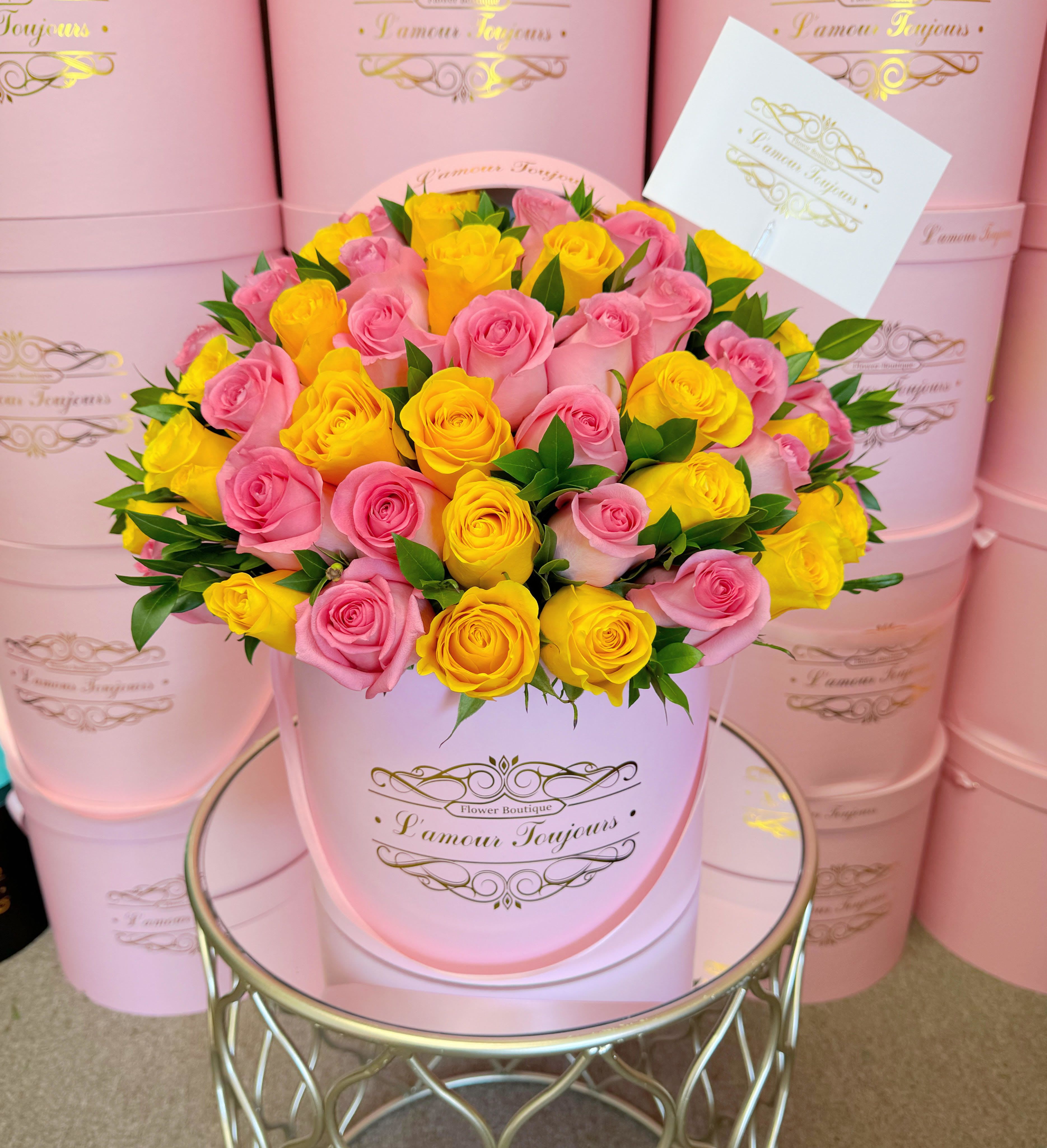 Round pink hatbox filled with pink and yellow roses and a card on a mirrored table