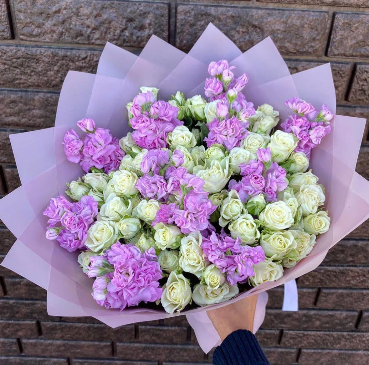 Hand-tied bouquet of cream spray roses and light lavender blooms wrapped in soft pink paper