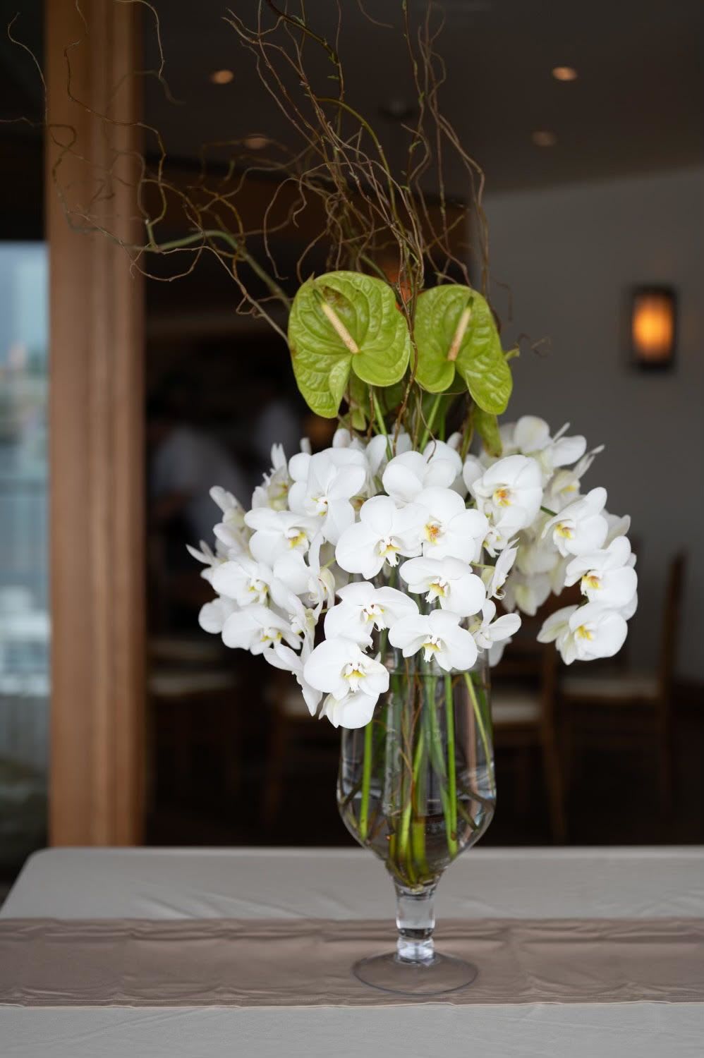 White orchids arranged in a clear glass vase with green anthurium accents