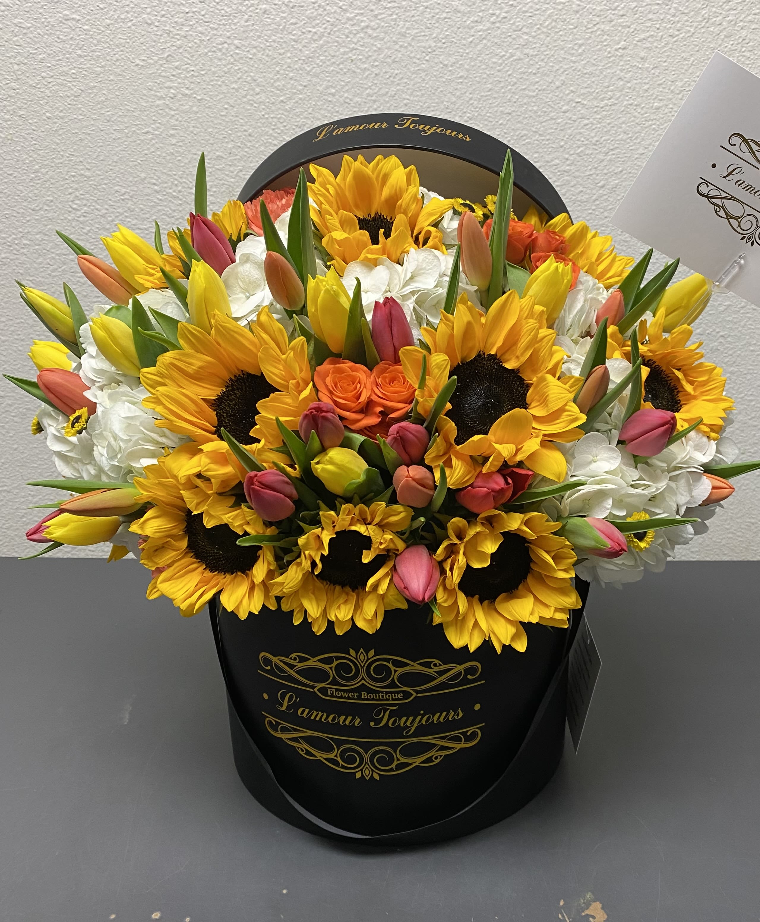 Bouquet of sunflowers, tulips, and white hydrangeas in a black hat box