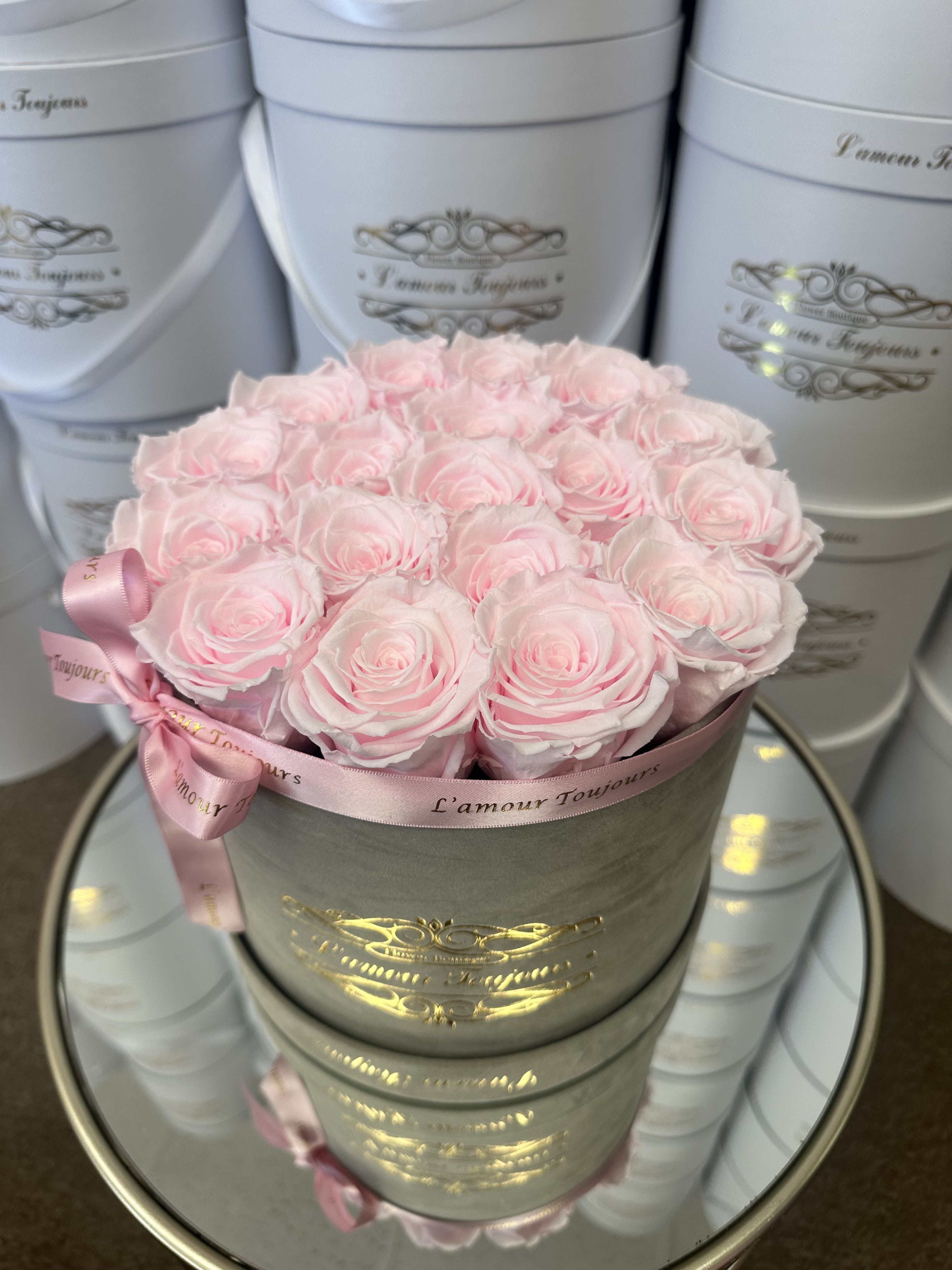 Round gray hat box filled with tightly packed light pink roses and tied with a pink ribbon.
