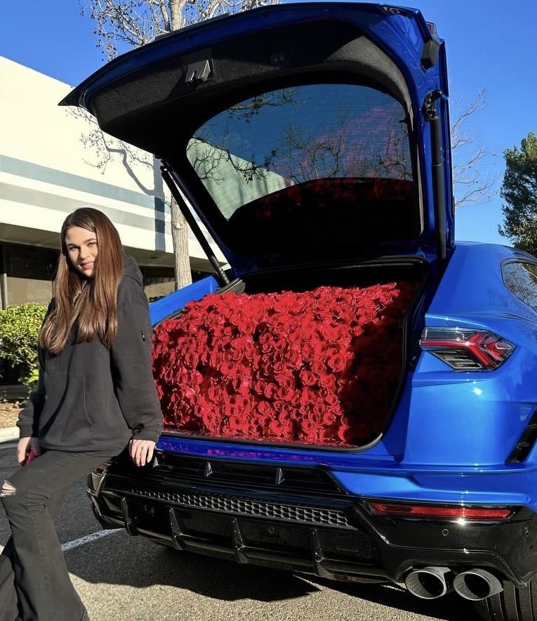 Blue SUV with its trunk filled with red roses beside a woman