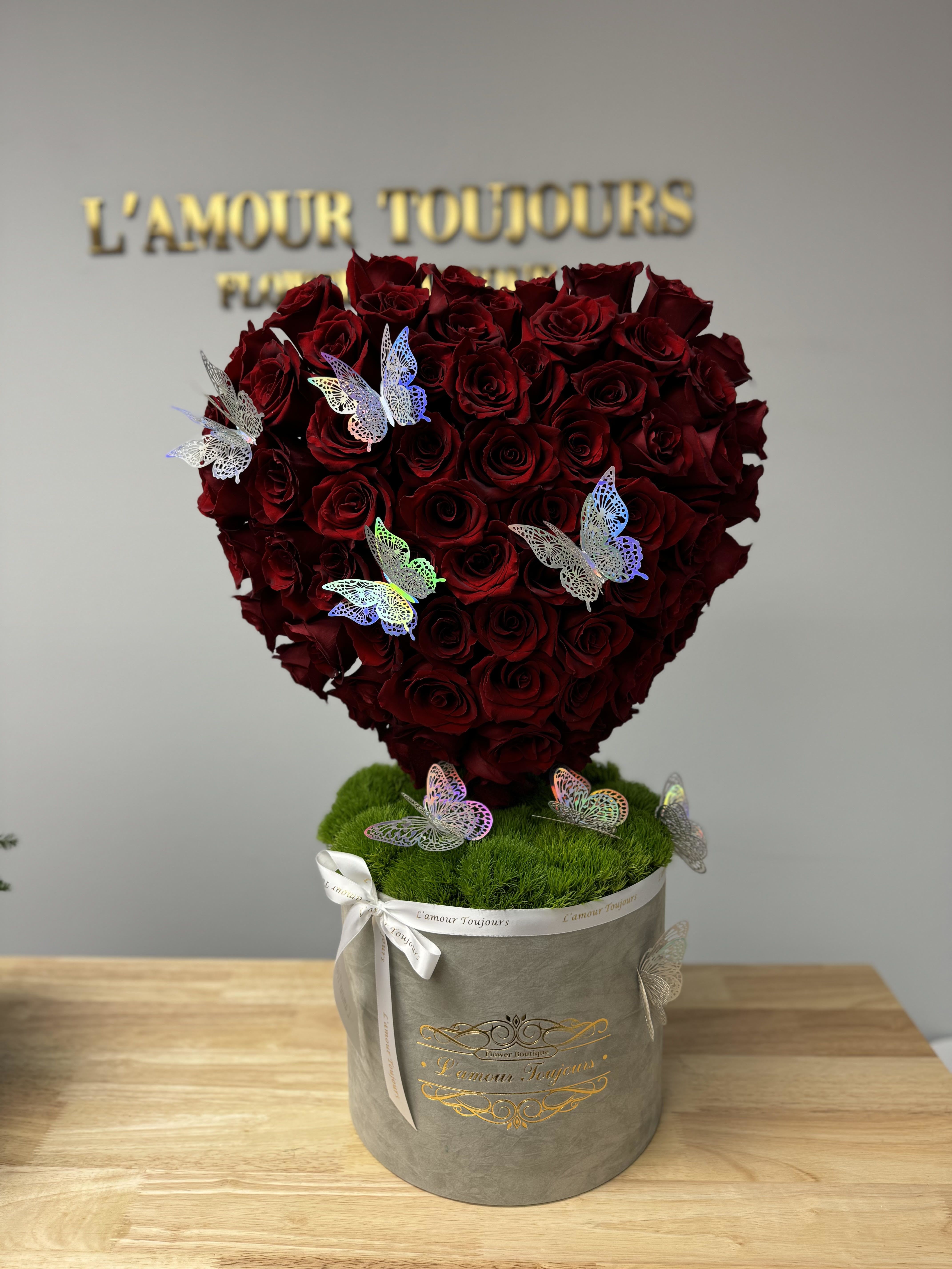Heart-shaped bouquet of red roses in a gray box with butterfly decorations