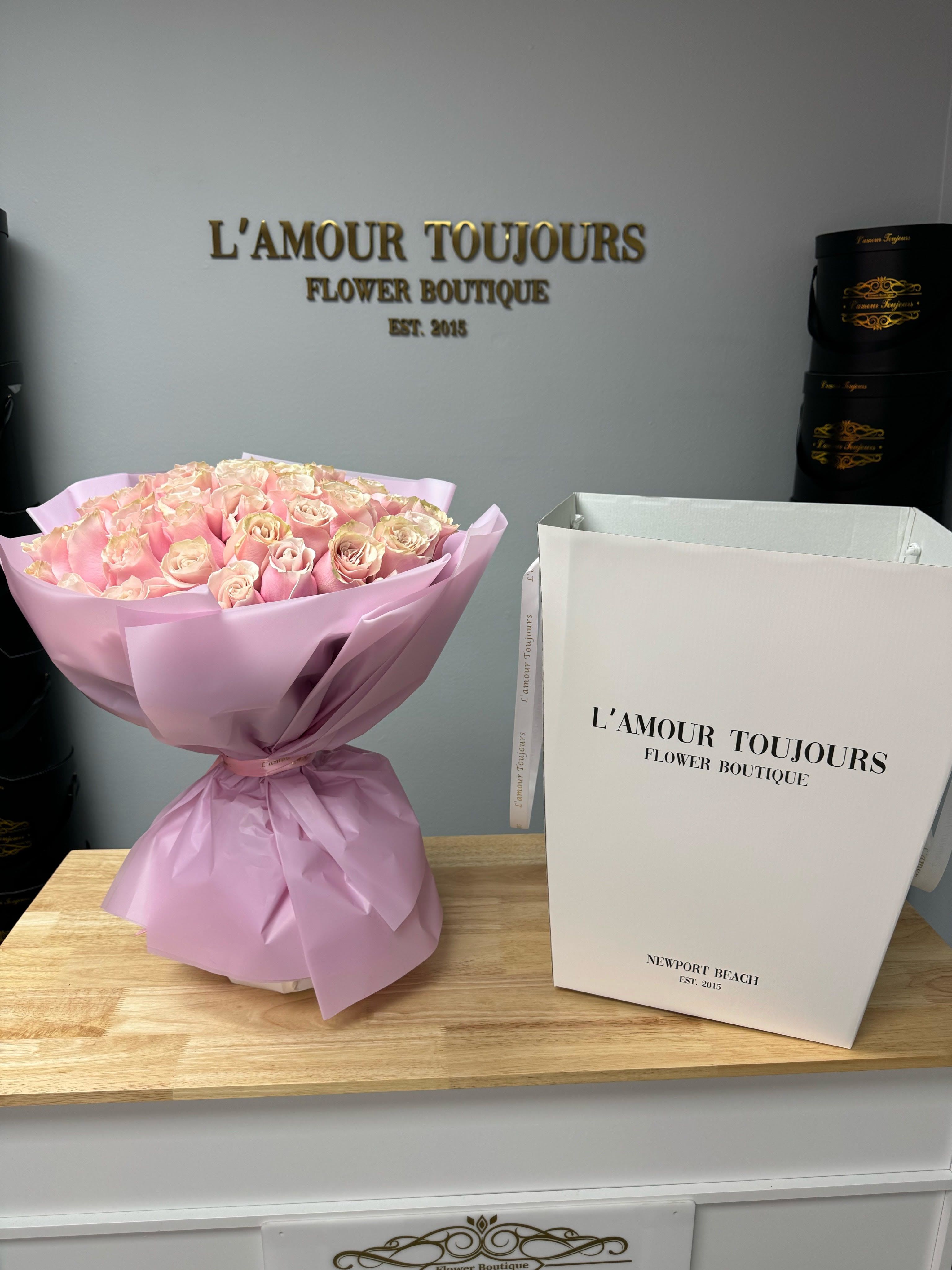 Pink rose bouquet wrapped in pale pink paper next to a tall white gift box.