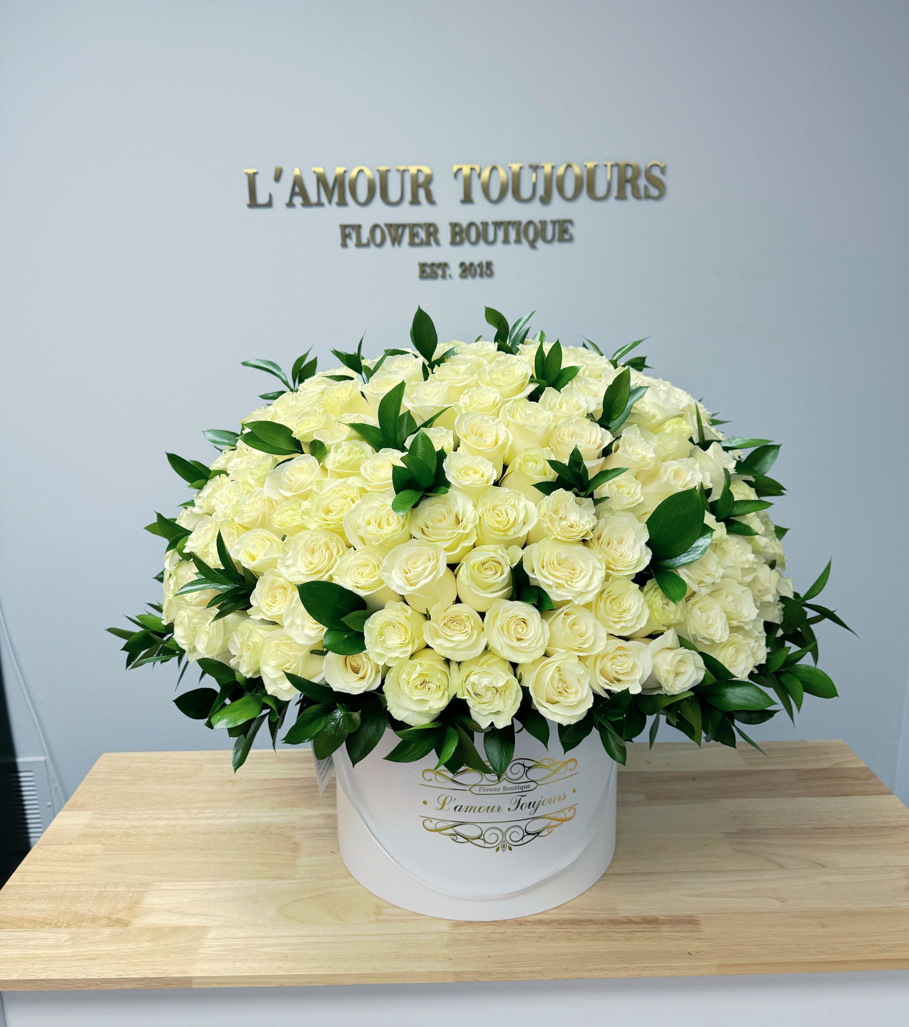 Large round hatbox of creamy white roses with dark green accents on a wooden table