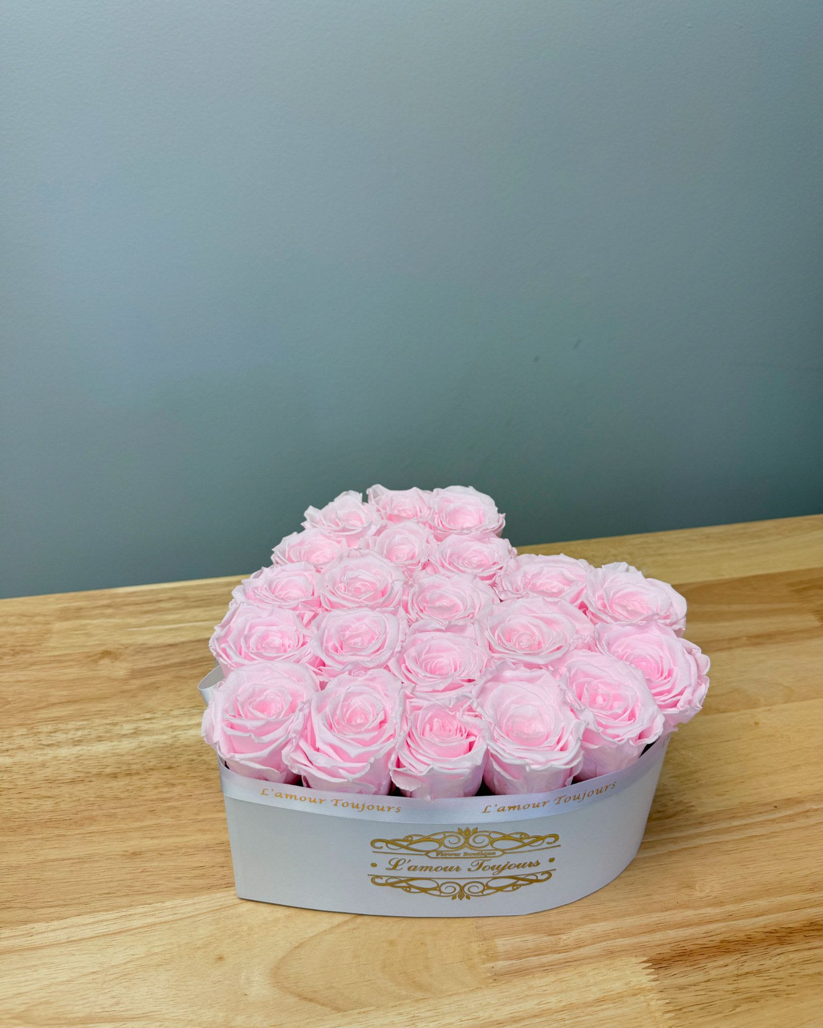 Pink roses arranged in a white heart-shaped box on a wooden table