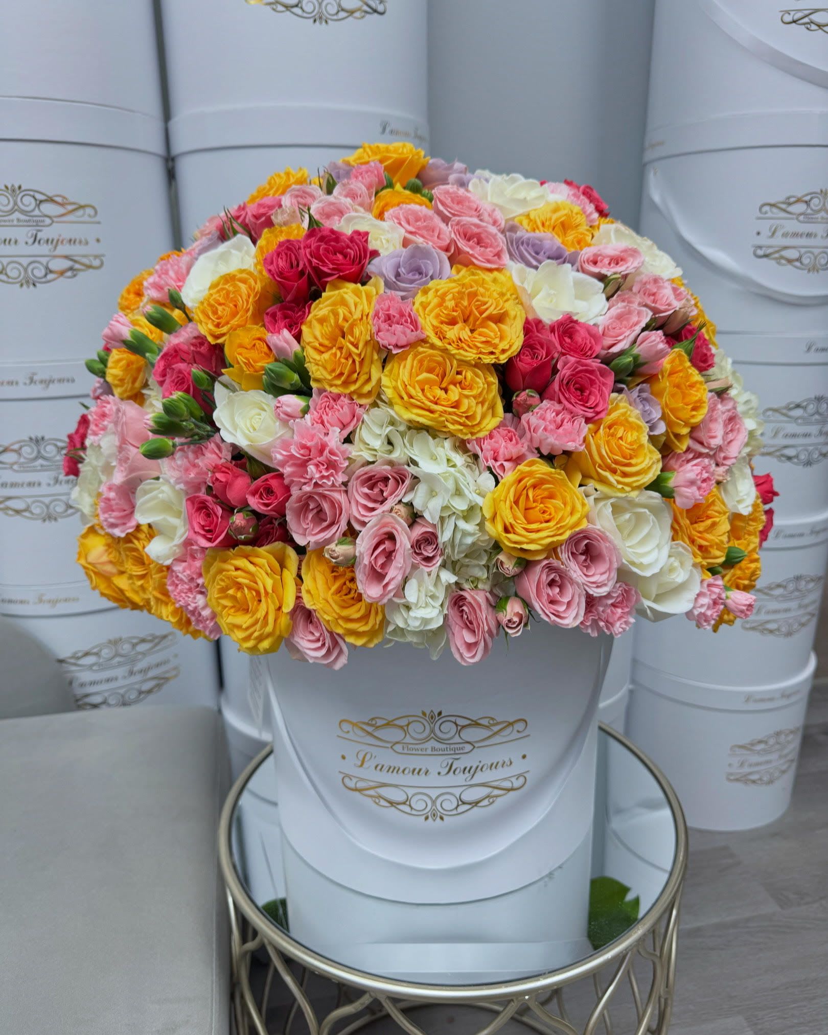 Round bouquet of pink, yellow, white, and lavender roses in a white hat box