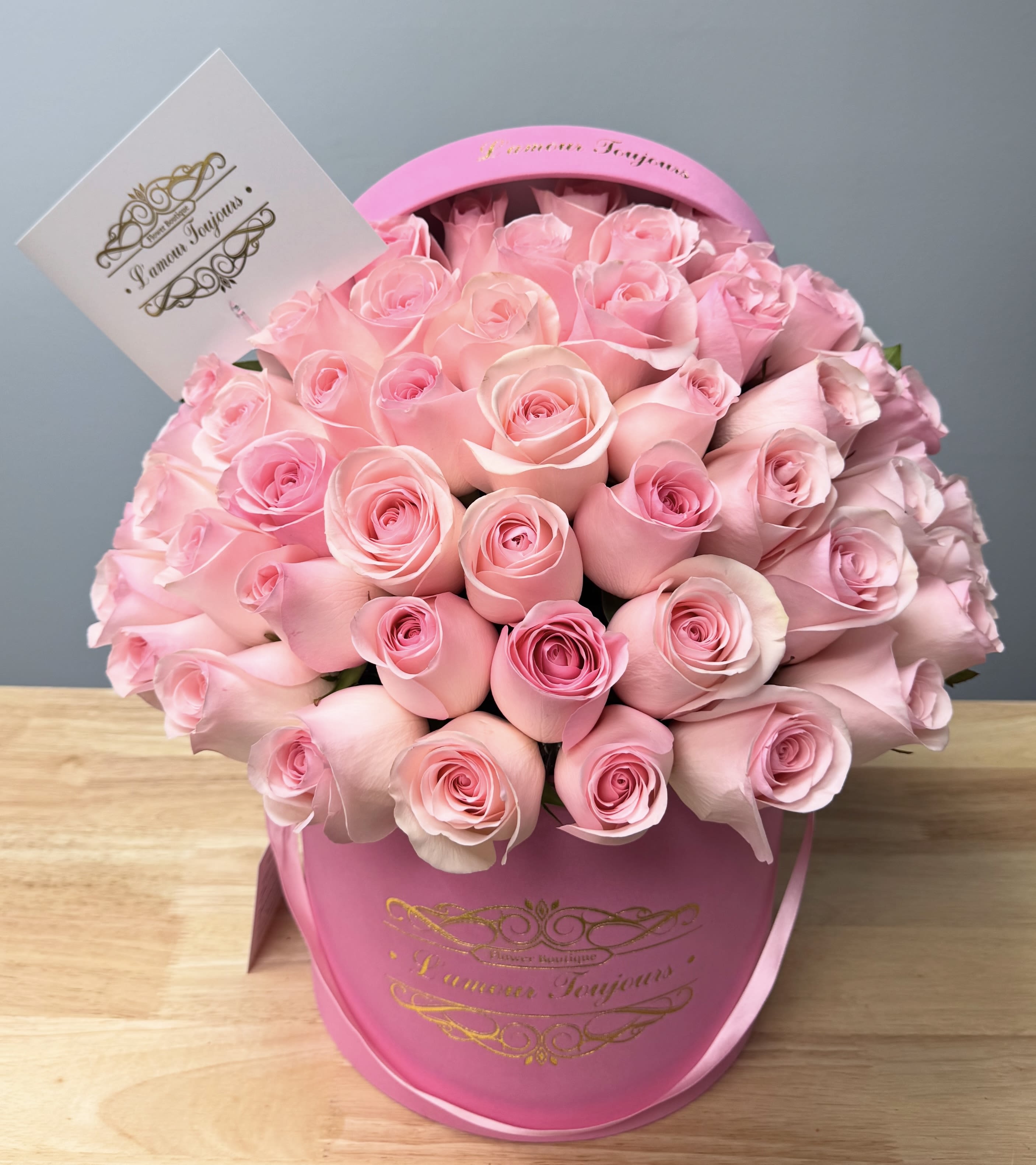 Pink roses arranged in a round pink hat box with a card attached