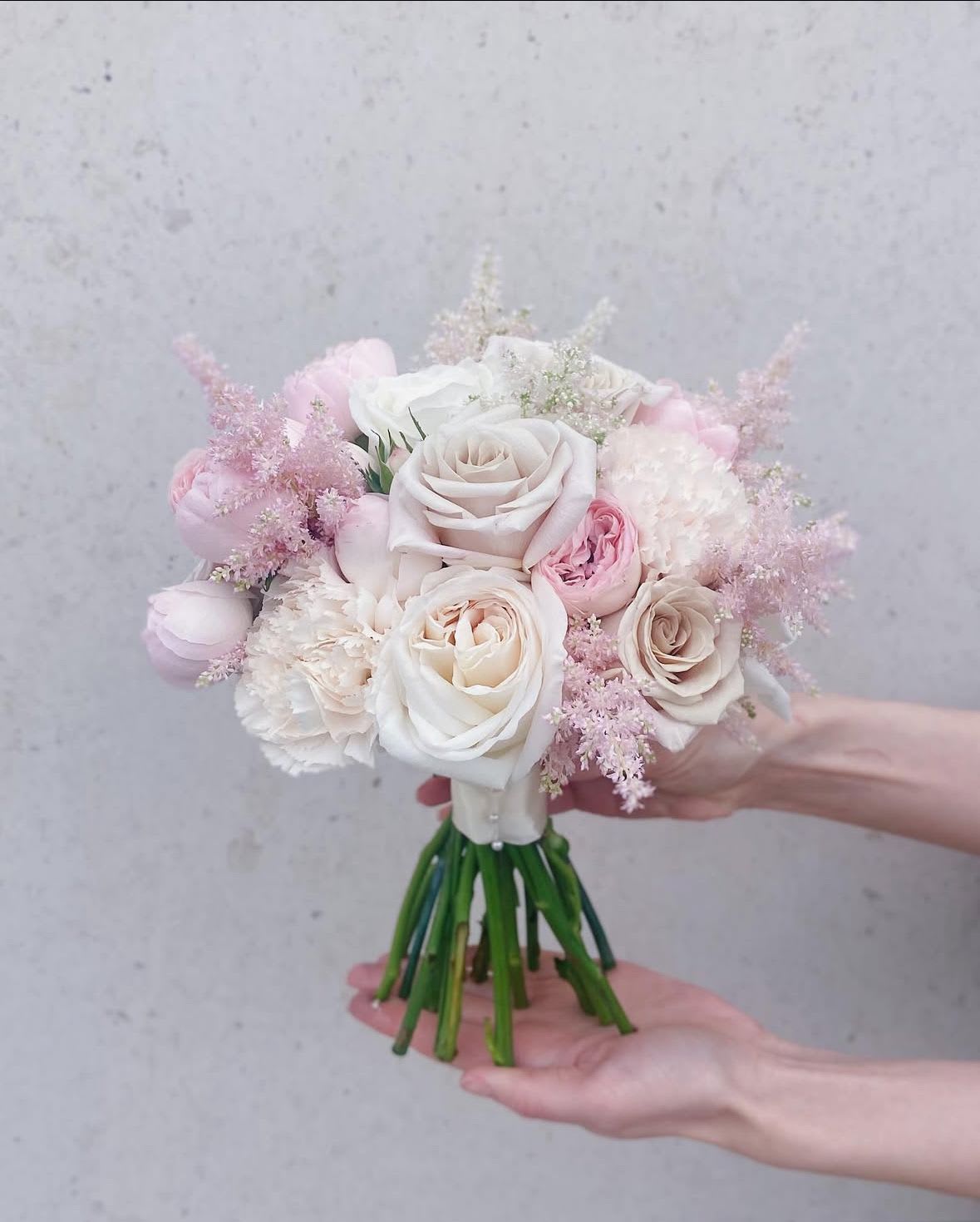 Handheld bouquet of pale pink and white roses with soft filler flowers