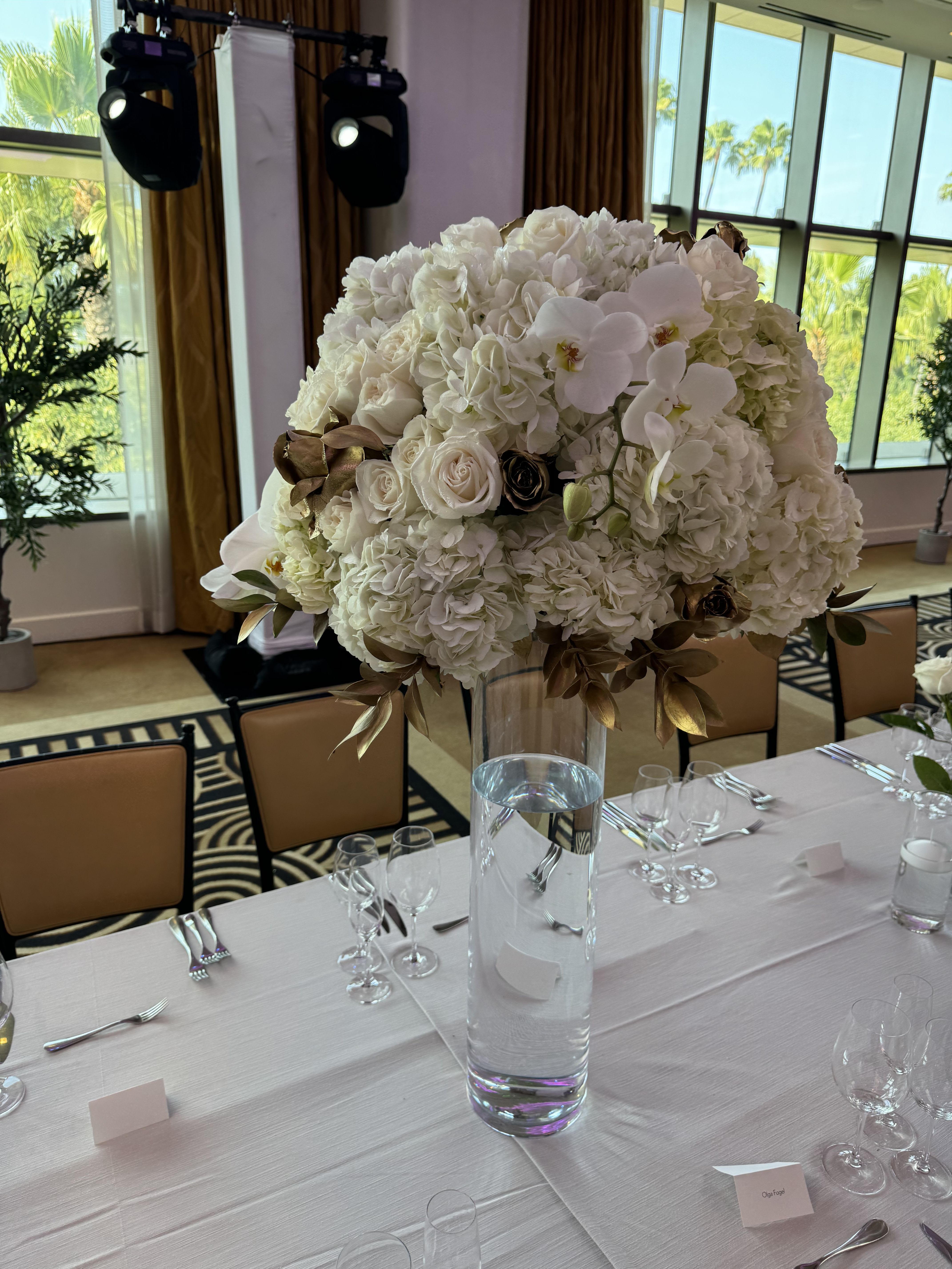 Large white floral centerpiece in a tall glass vase on a set dining table