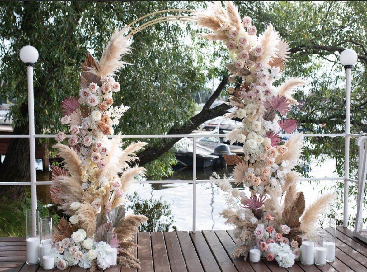 Tall floral arch with pastel roses and pampas grass beside white candles