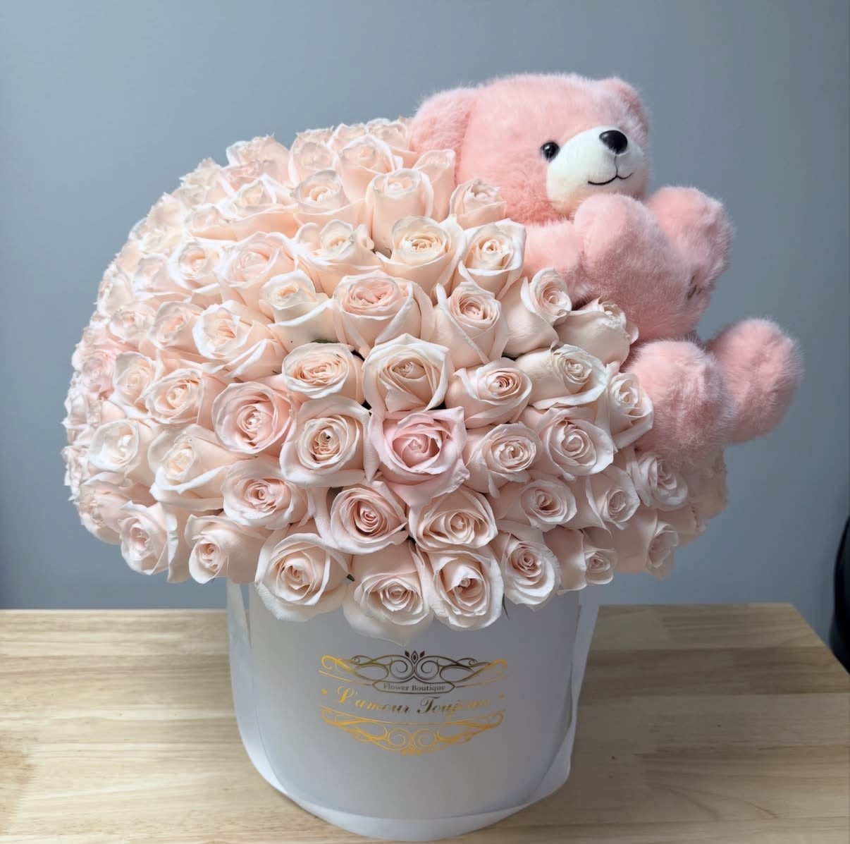 It's a Girl Signature Box - Pale blush roses arranged in a compact dome create an irresistibly soft focal point in this baby- or celebration-ready flower arrangement - perfect as a baby shower surprise or "welcome baby" gift. The white hat box and gentle pink-and-white palette read as both classic and modern, making this flower arrangement ideal for new moms, a birthday for someone who loves romantic florals, or any moment when you want to say congratulations with sweetness.  The arrangement is composed of tightly packed pale blush roses set low in a crisp white hat box so the blooms read like a luxe, velvety cushion. A plush pink teddy bear is tucked into the upper right side for an added keepsake and playful touch, turning the presentation into a two-part gift that feels polished and gift-ready. The compact dome shape keeps the design neat for tabletops or nursery displays while emphasizing the roses' soft texture and gentle color story.  Send this to the person you want to make feel seen and celebrated - it conveys warmth, tenderness, and thoughtful attention to detail. Available in the pictured white hat box with the tucked-in teddy bear, the arrangement is easy to place in any room; keep the roses in fresh water and out of direct sun for longer enjoyment.