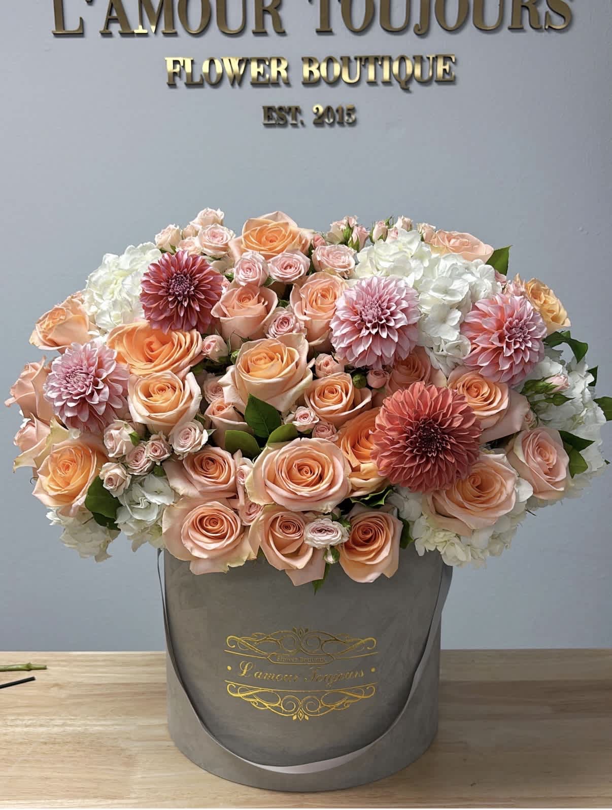 Peach and pink roses with white hydrangeas in a gray hatbox
