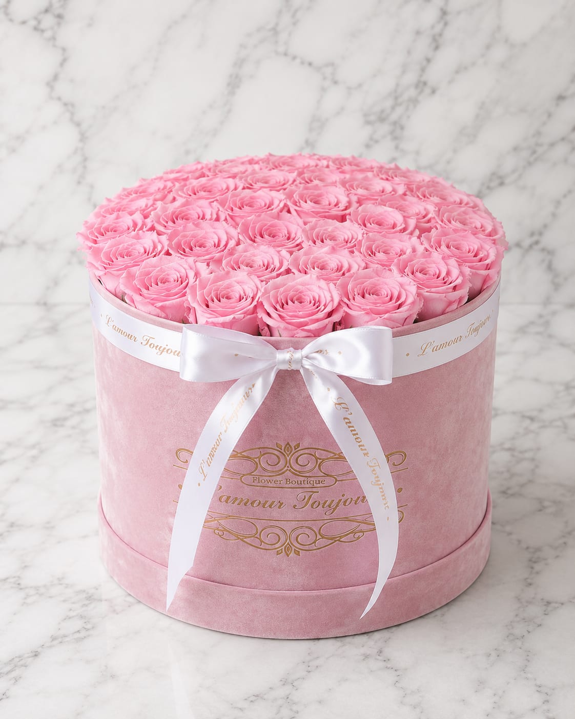 Round pink box filled with pink roses and tied with a white ribbon