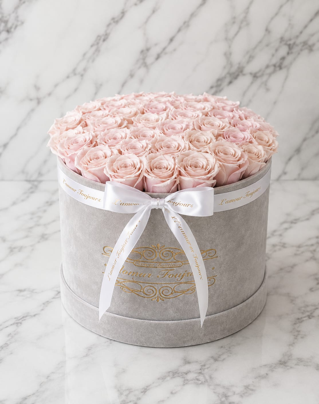 Round box of pale pink roses tied with a white ribbon