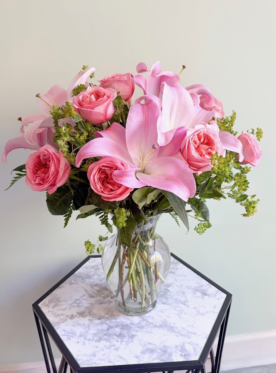 Pink lilies - Soft, romantic, and  elegant, this arrangement features delicate pink lilies paired with lush pink garden roses. The lilies bloom with graceful petals and a light, sweet fragrance, while the garden roses add a full, ruffled texture and classic charm. Together, they create a harmonious blend of softness and sophistication—perfect for celebrating love, expressing gratitude, or brightening any space with a gentle touch of beauty.