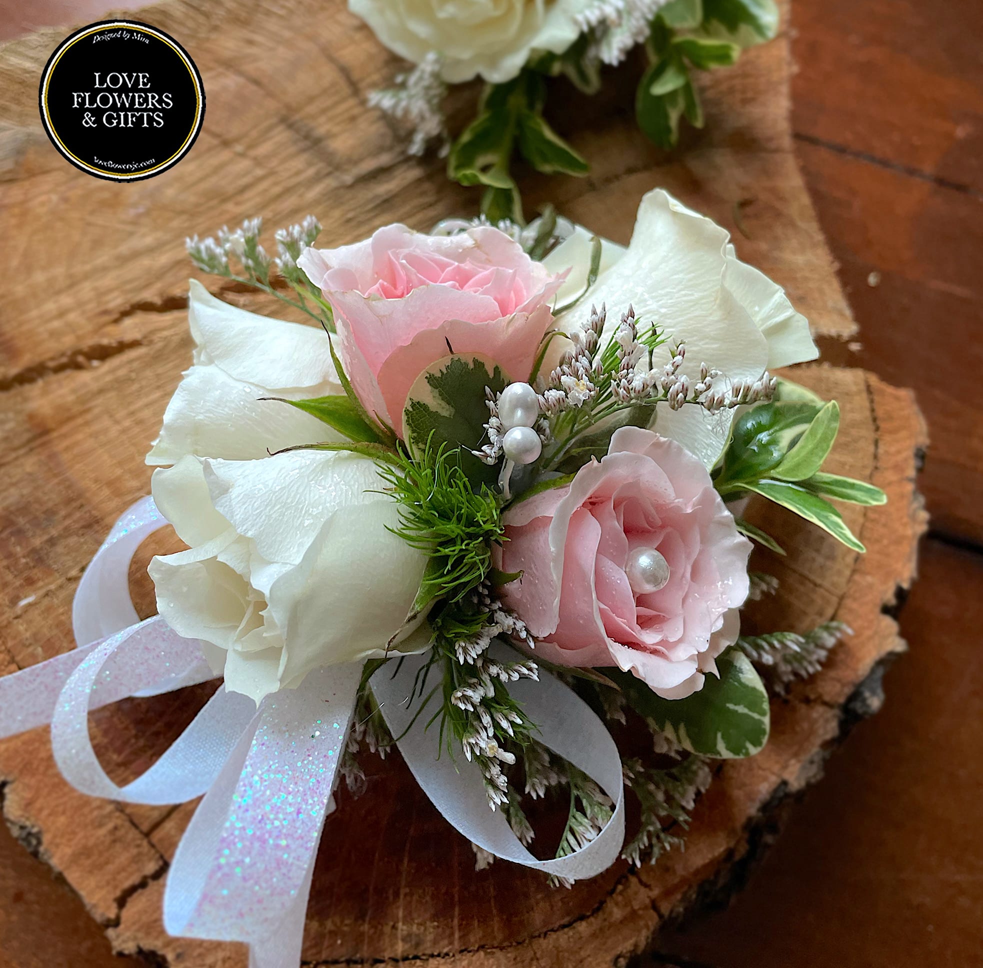 Pink and white rose wrist corsage with ribbon and pearl accents on a wood slice