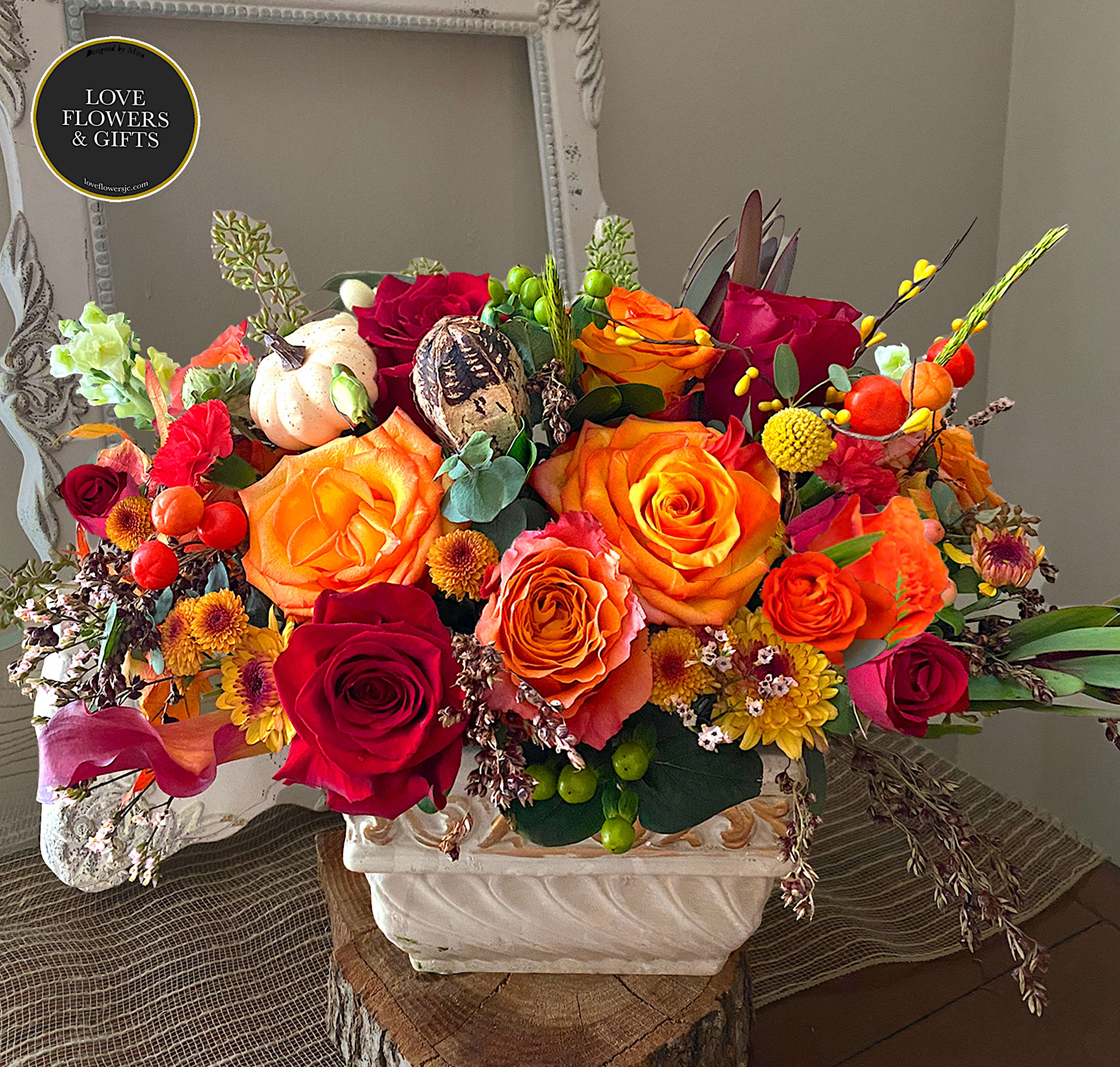 Low arrangement of orange and red roses with yellow accents in a white rectangular vase