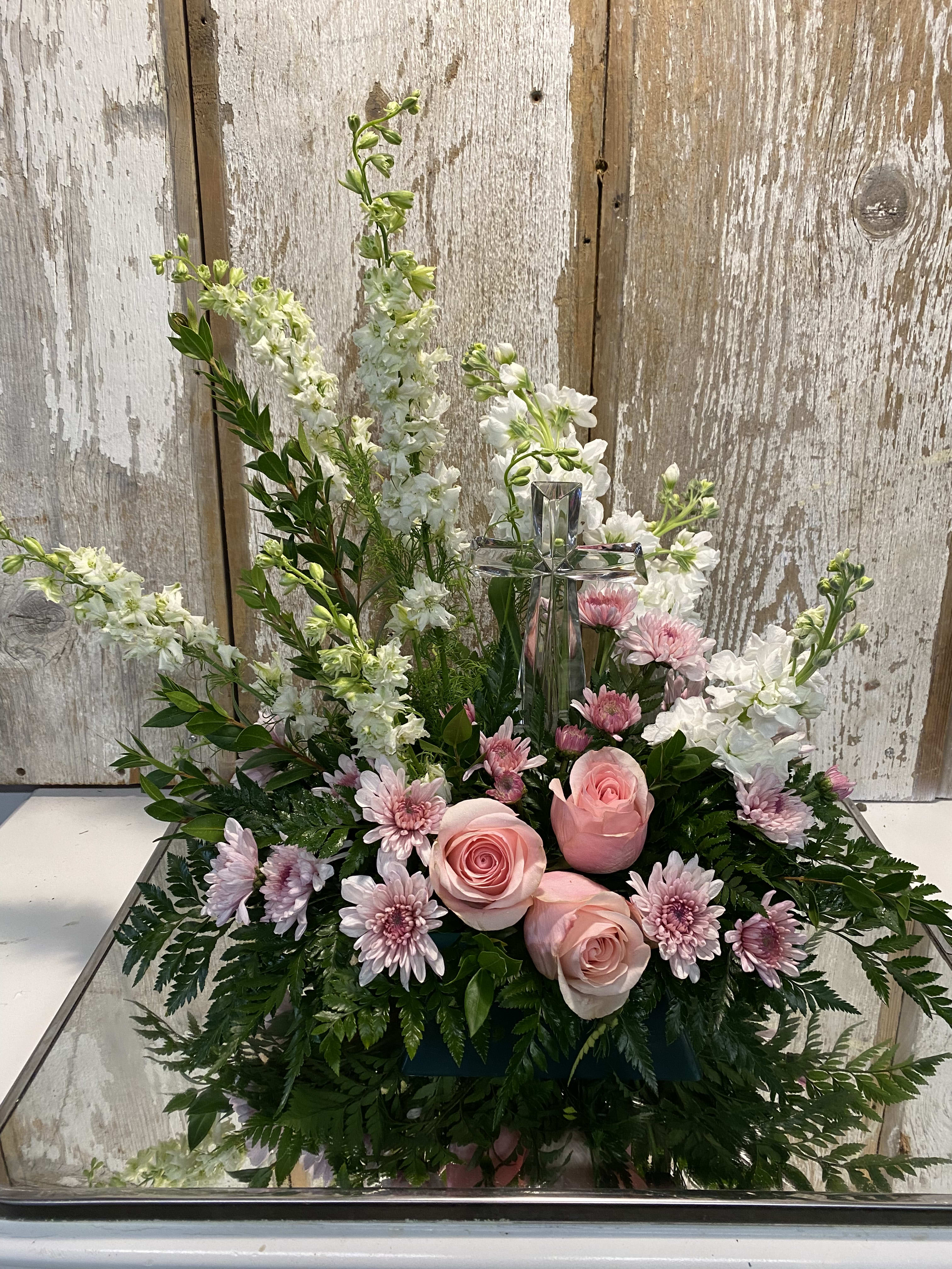 Pink roses and white flowers arranged around a glass cross