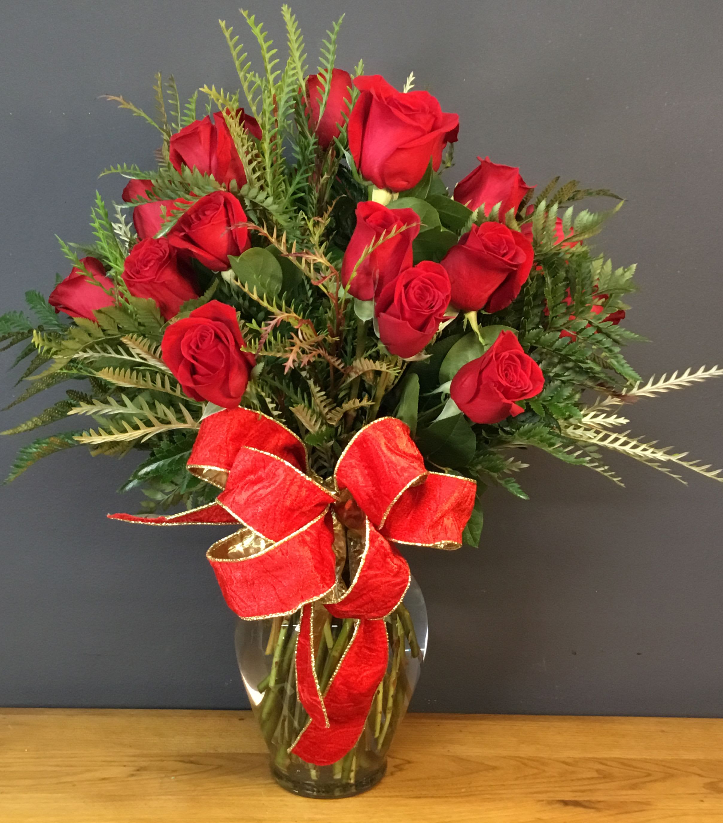 Red roses arranged in a glass vase with a red ribbon bow