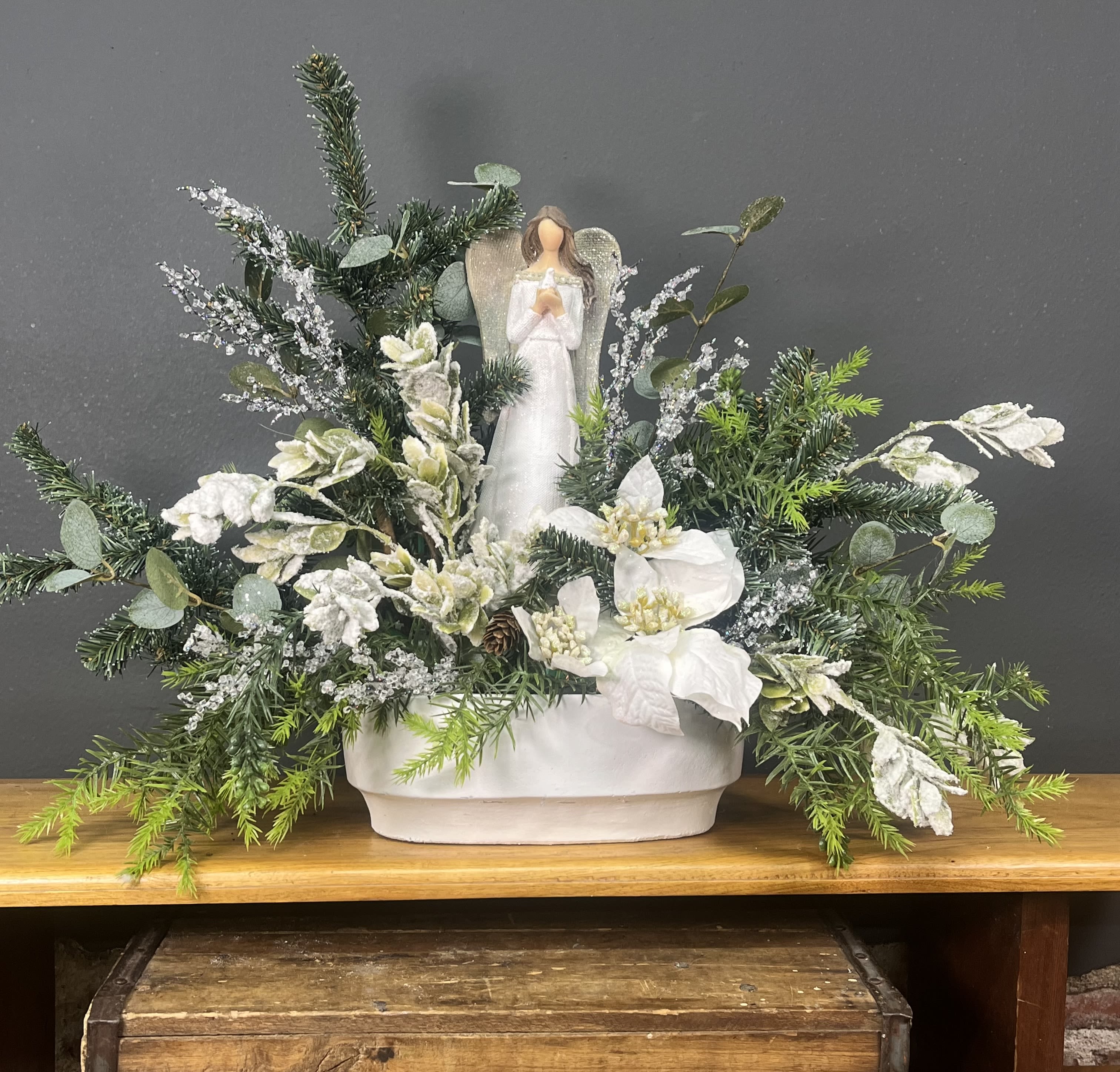 Winter floral arrangement with a small angel figurine in a white container