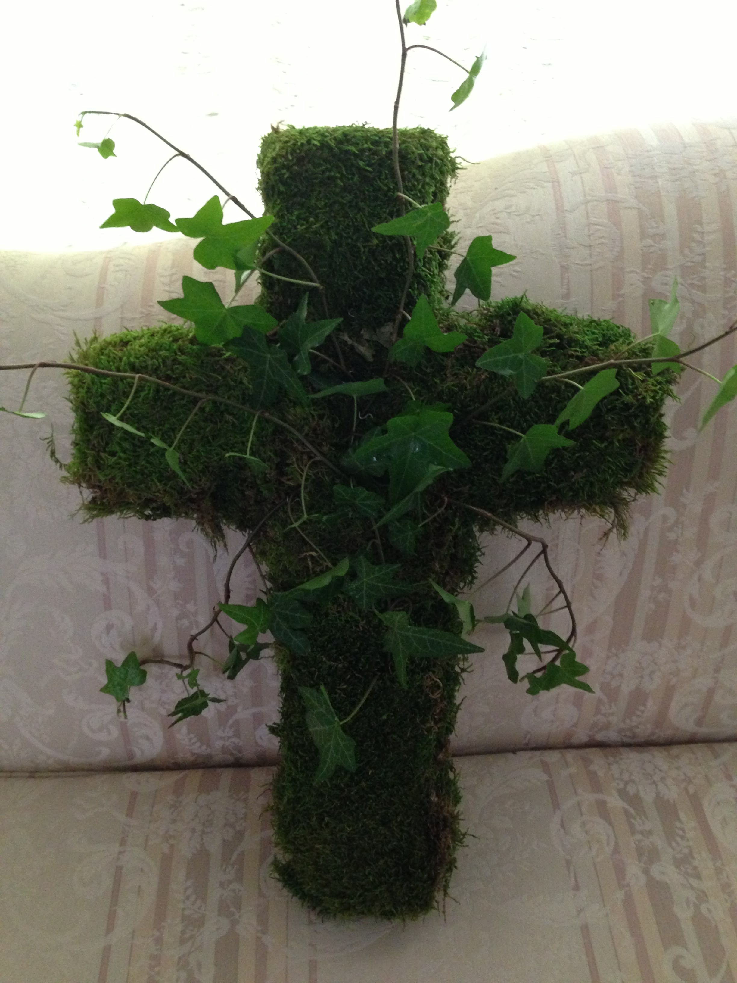 Moss-covered cross with trailing ivy on a patterned sofa